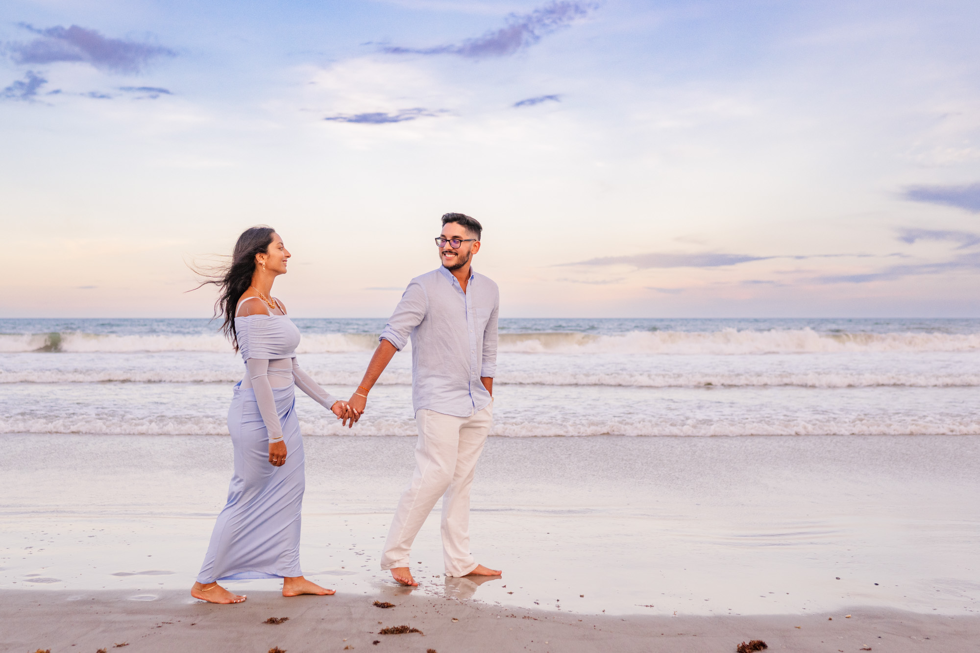 Man and woman holding hands while walking along the edge of the ocean