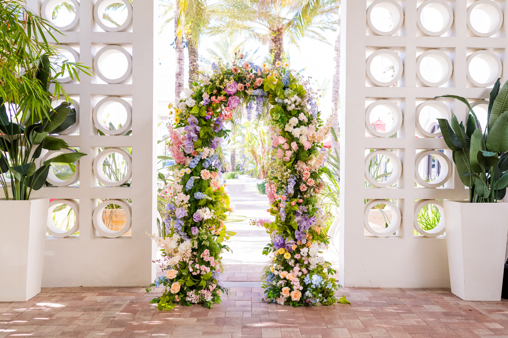 Colorful floral wedding arch framed by the modern circular wall at Costa d’Este in Vero Beach.