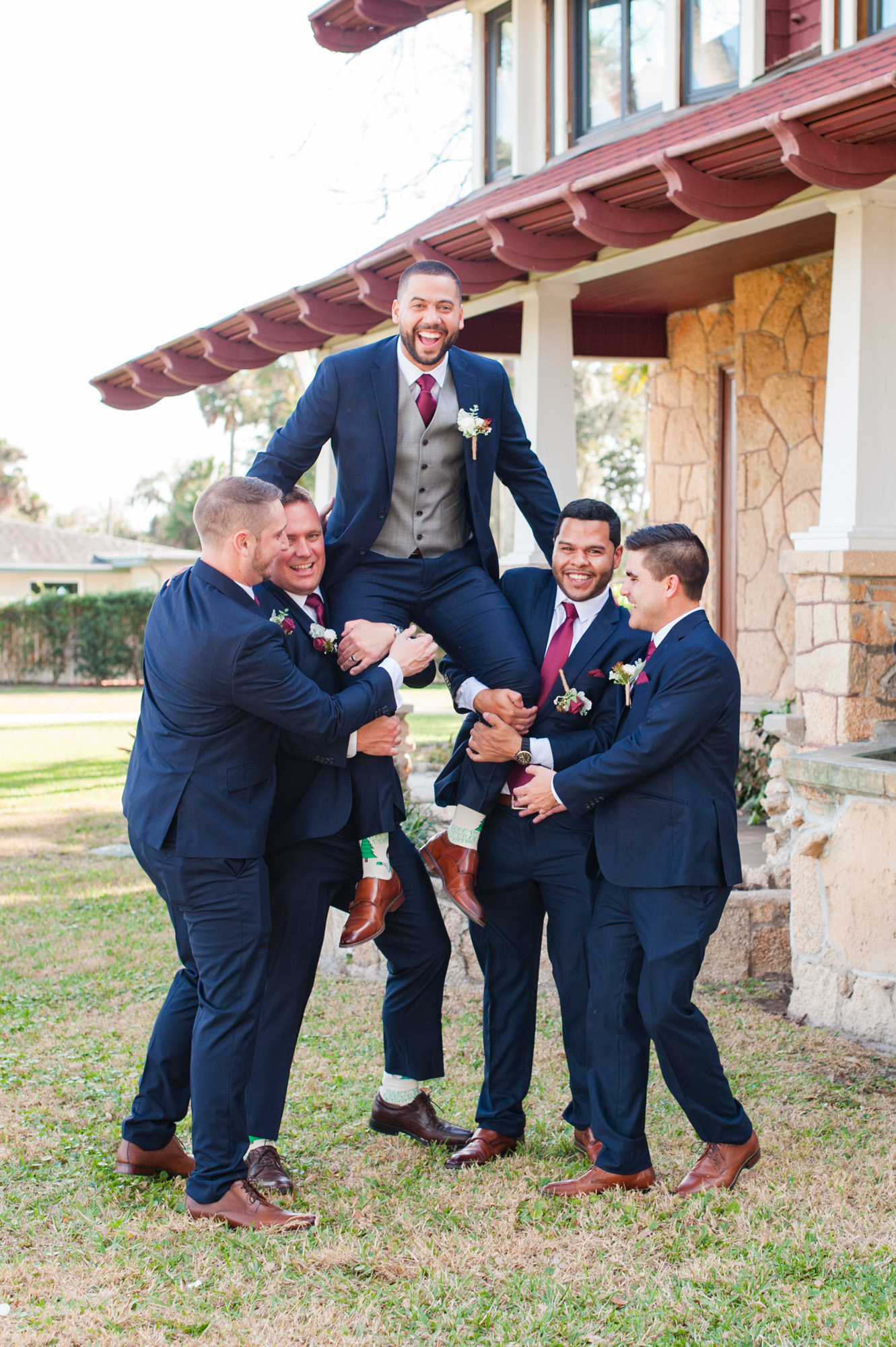 Groomsmen lifting the groom in the air during a playful wedding party portrait.