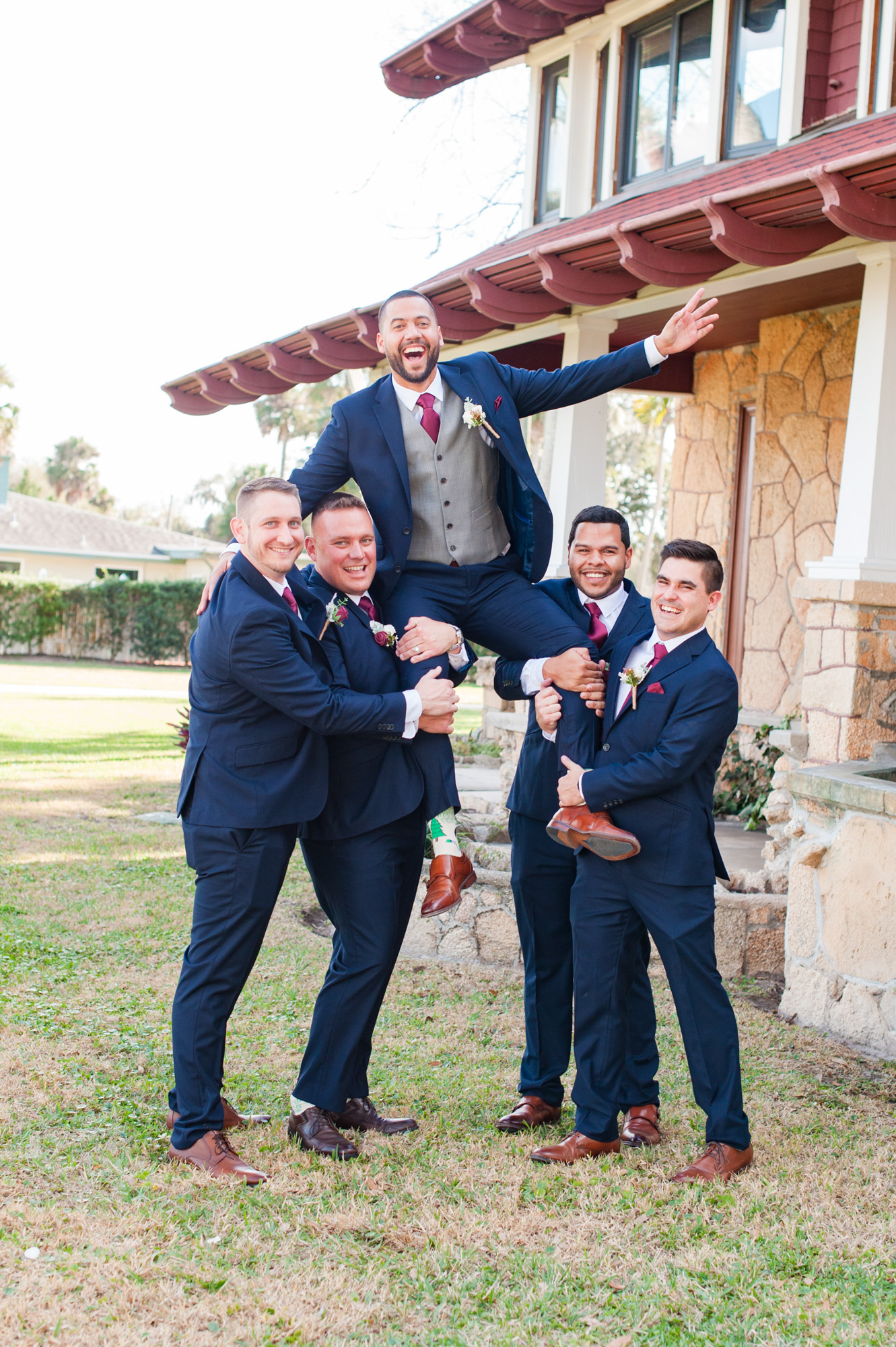 Groomsmen lifting the groom while laughing together outside Estate on the Halifax.
