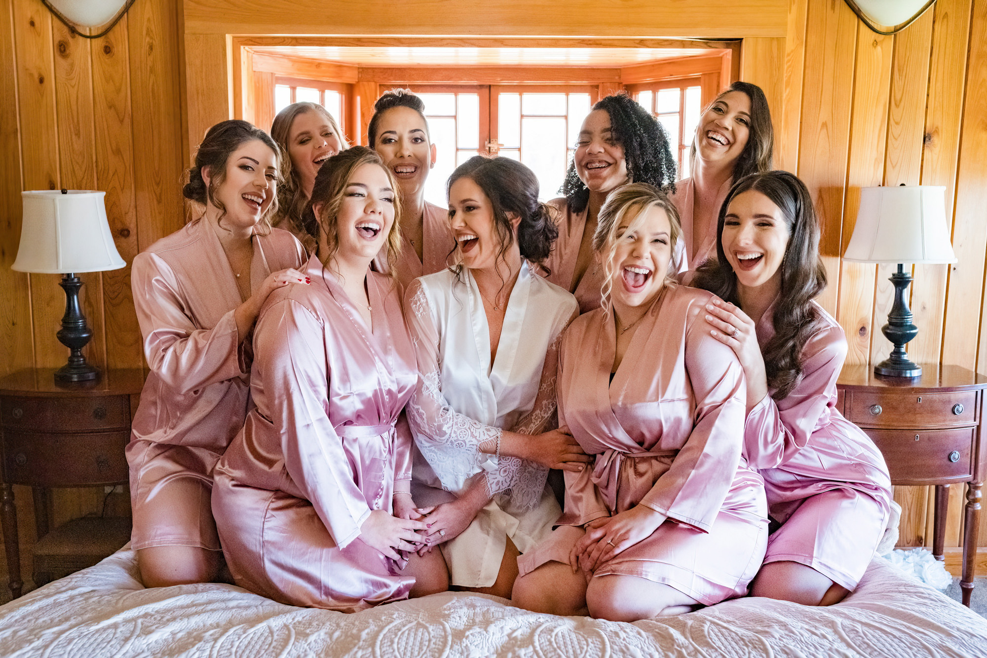 Bride laughing with her bridesmaids in matching pink robes before the wedding ceremony.