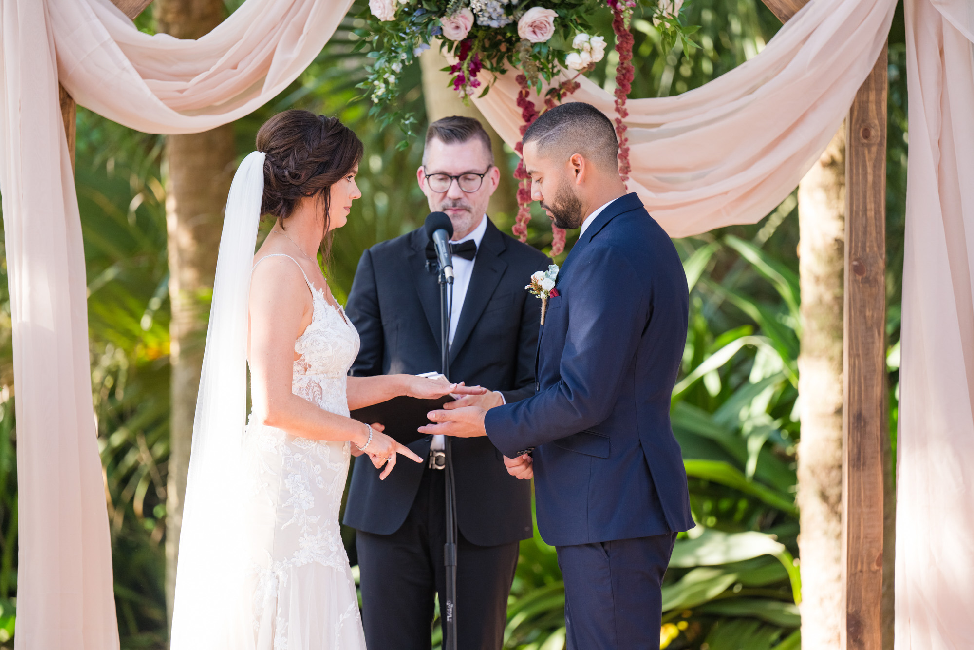 Groom placing a wedding ring on the bride’s hand during their outdoor ceremony.