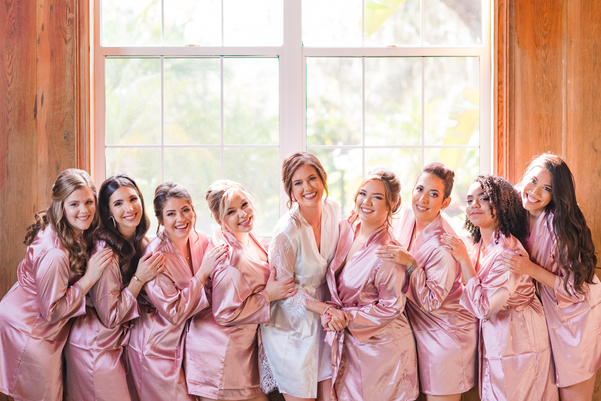 Bride laughing with her bridesmaids in matching pink robes before the wedding ceremony.