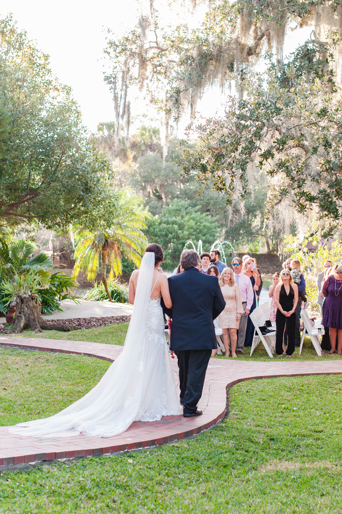 Bride walking with her father along the brick path toward the outdoor ceremony.