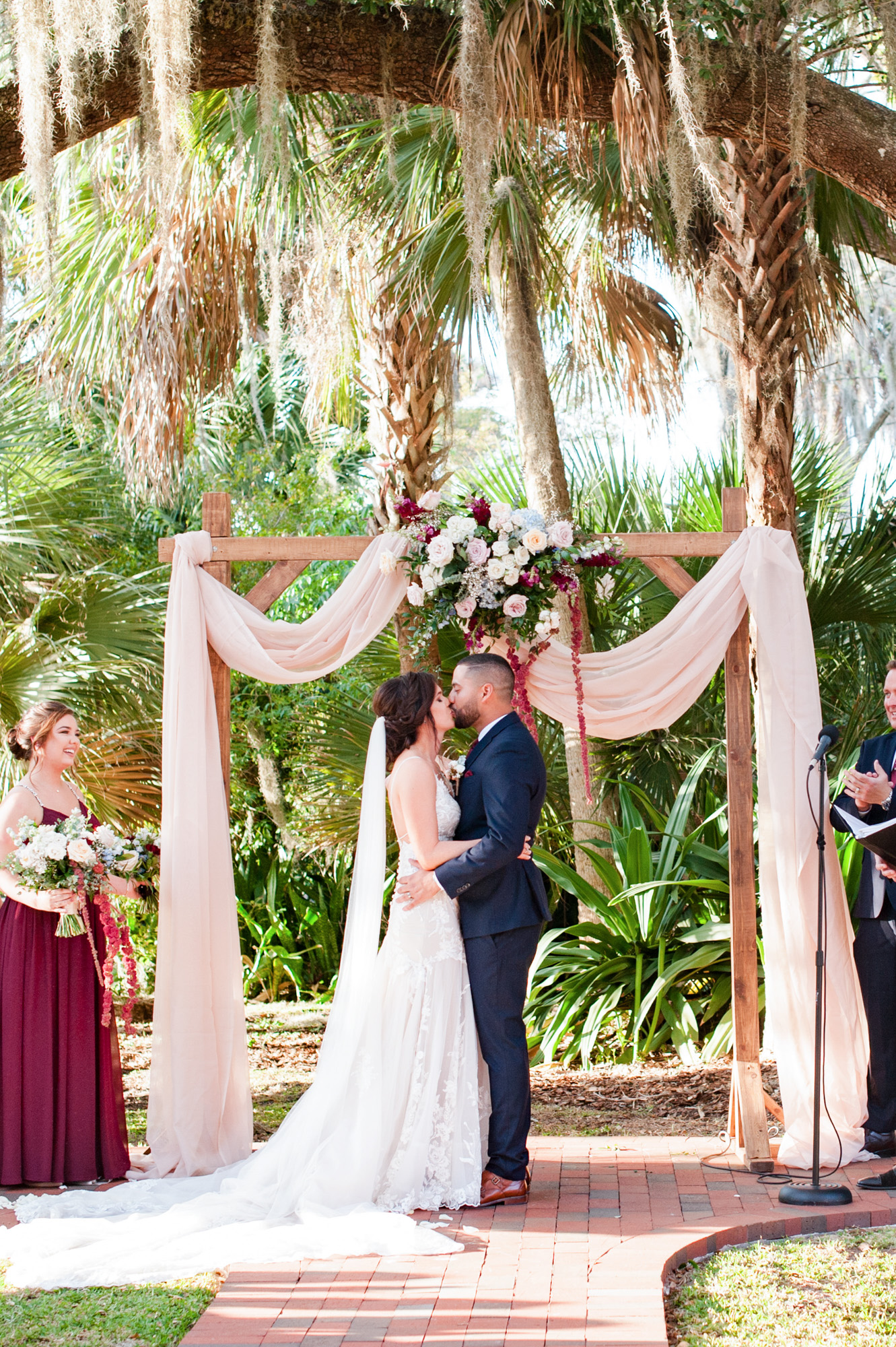 Newlyweds kissing beneath the floral wedding arch during their outdoor ceremony.