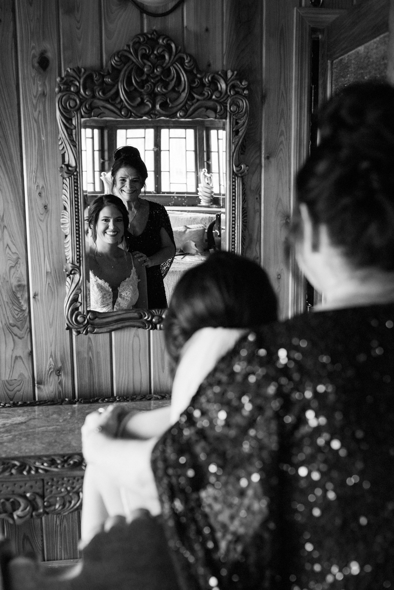 Bride smiling at her reflection while getting ready with a family member before the wedding.
