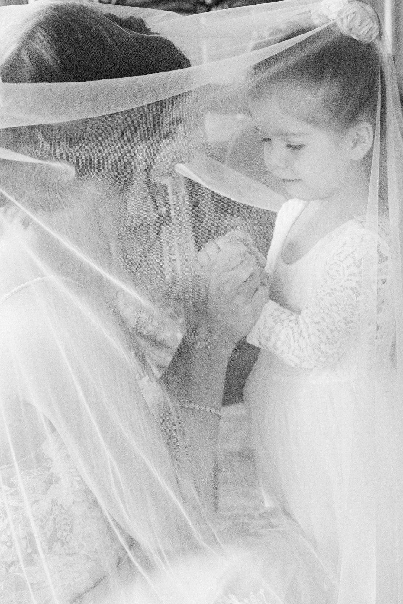 Bride sharing a sweet moment under her veil with a young flower girl.