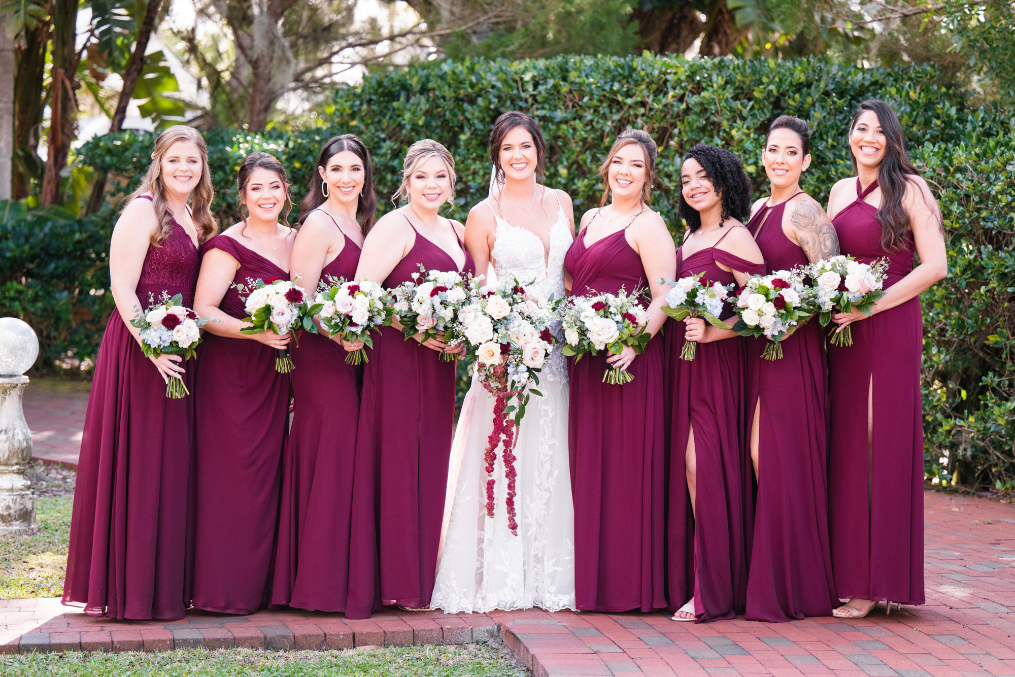 Bride and bridesmaids posing together in burgundy dresses with coordinating bouquets.