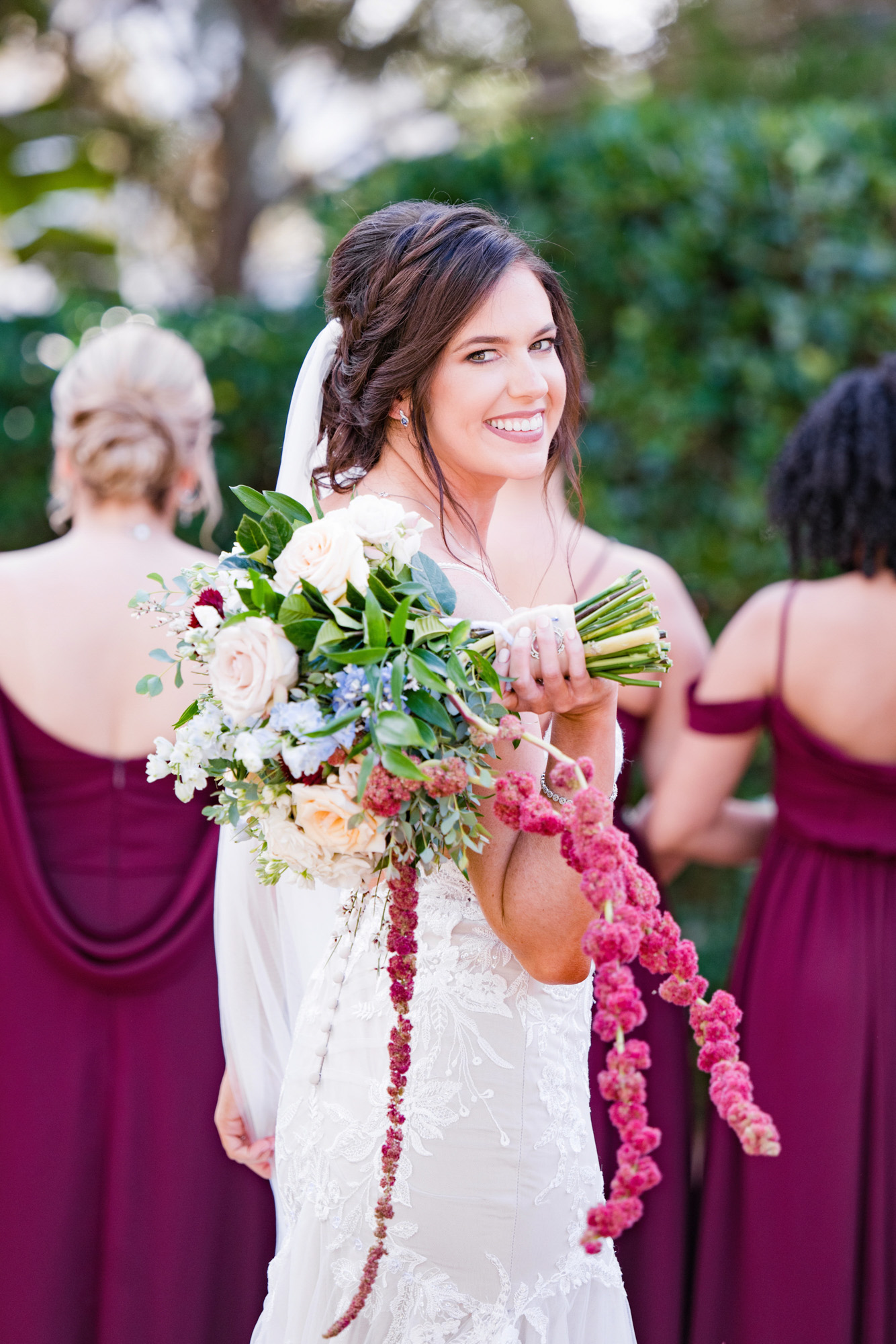 Bride smiling while holding her cascading bouquet during wedding party portraits.