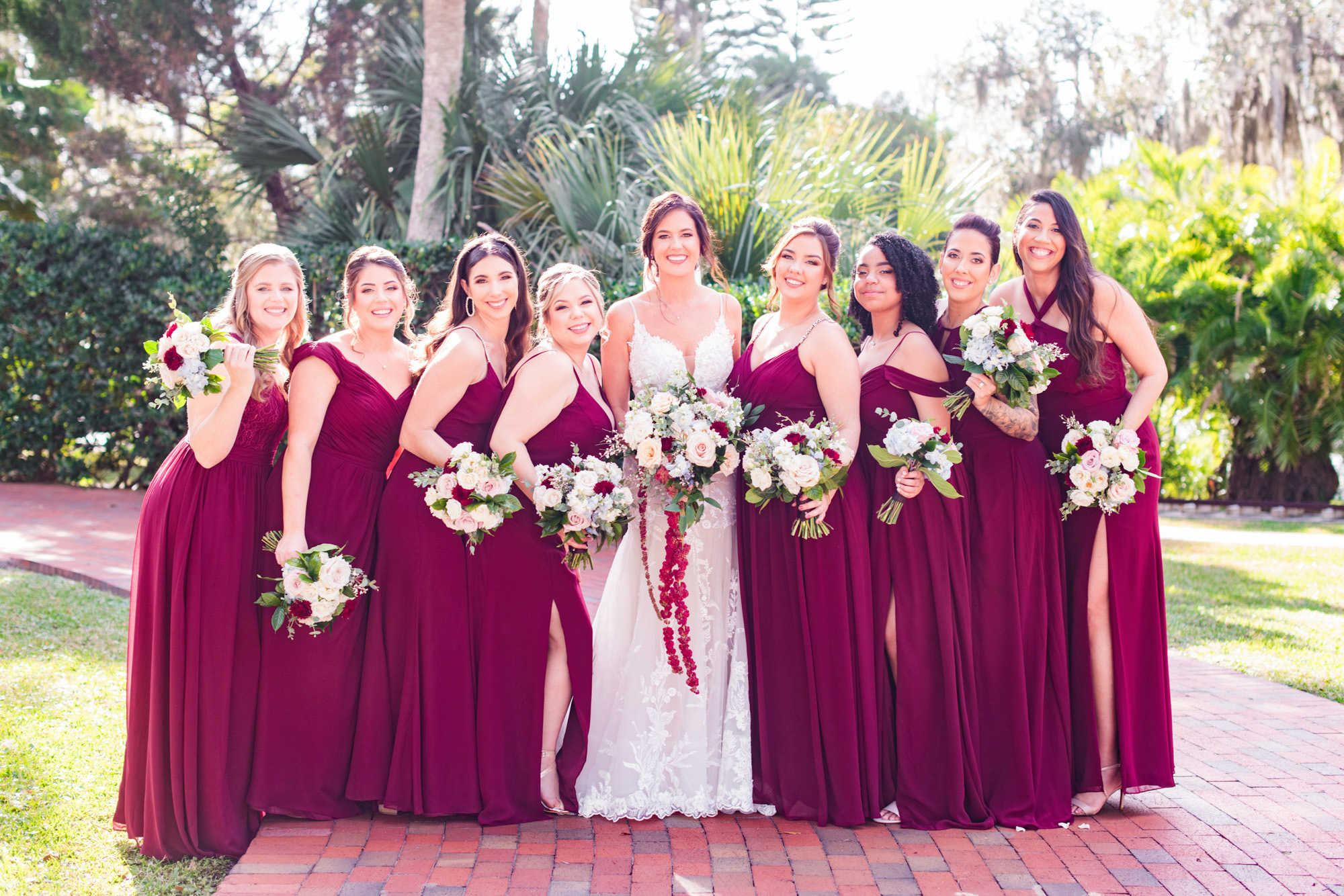 Bride and bridesmaids posing together outdoors in burgundy dresses at Estate on the Halifax.