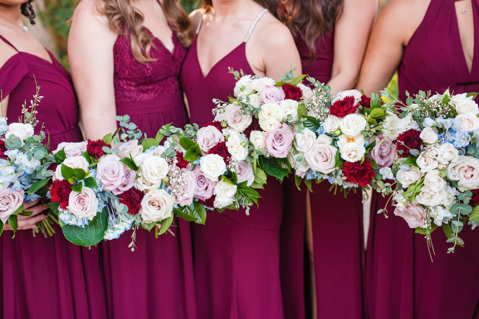 Close-up of bridesmaids holding blush, white, burgundy and blue wedding bouquets.