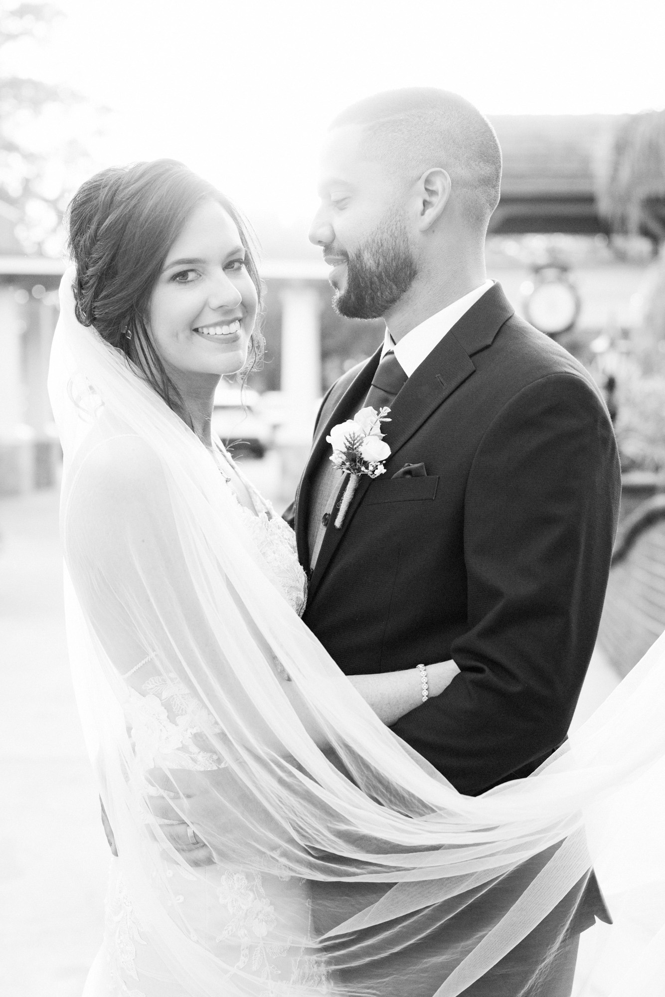 Black-and-white portrait of the bride and groom wrapped in the bride’s veil.