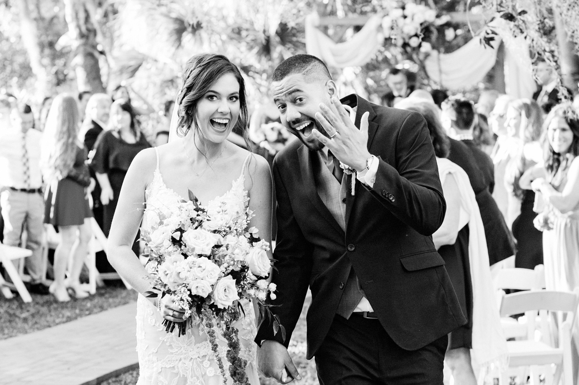 Black-and-white candid of the newlyweds celebrating after their outdoor wedding ceremony.