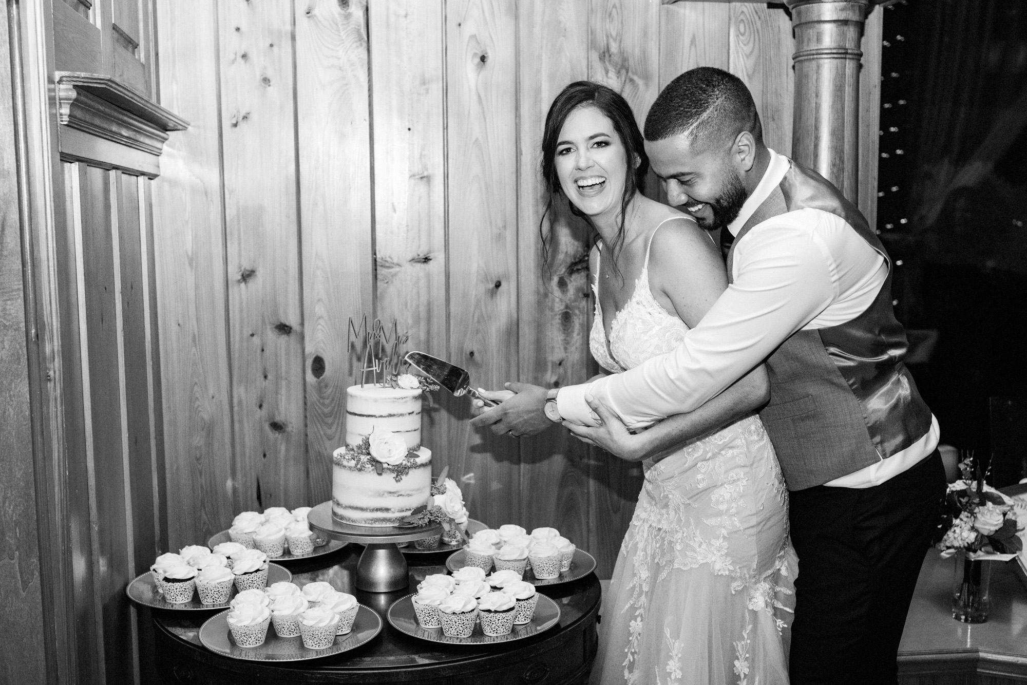 Bride and groom laughing together while cutting their wedding cake at the reception.