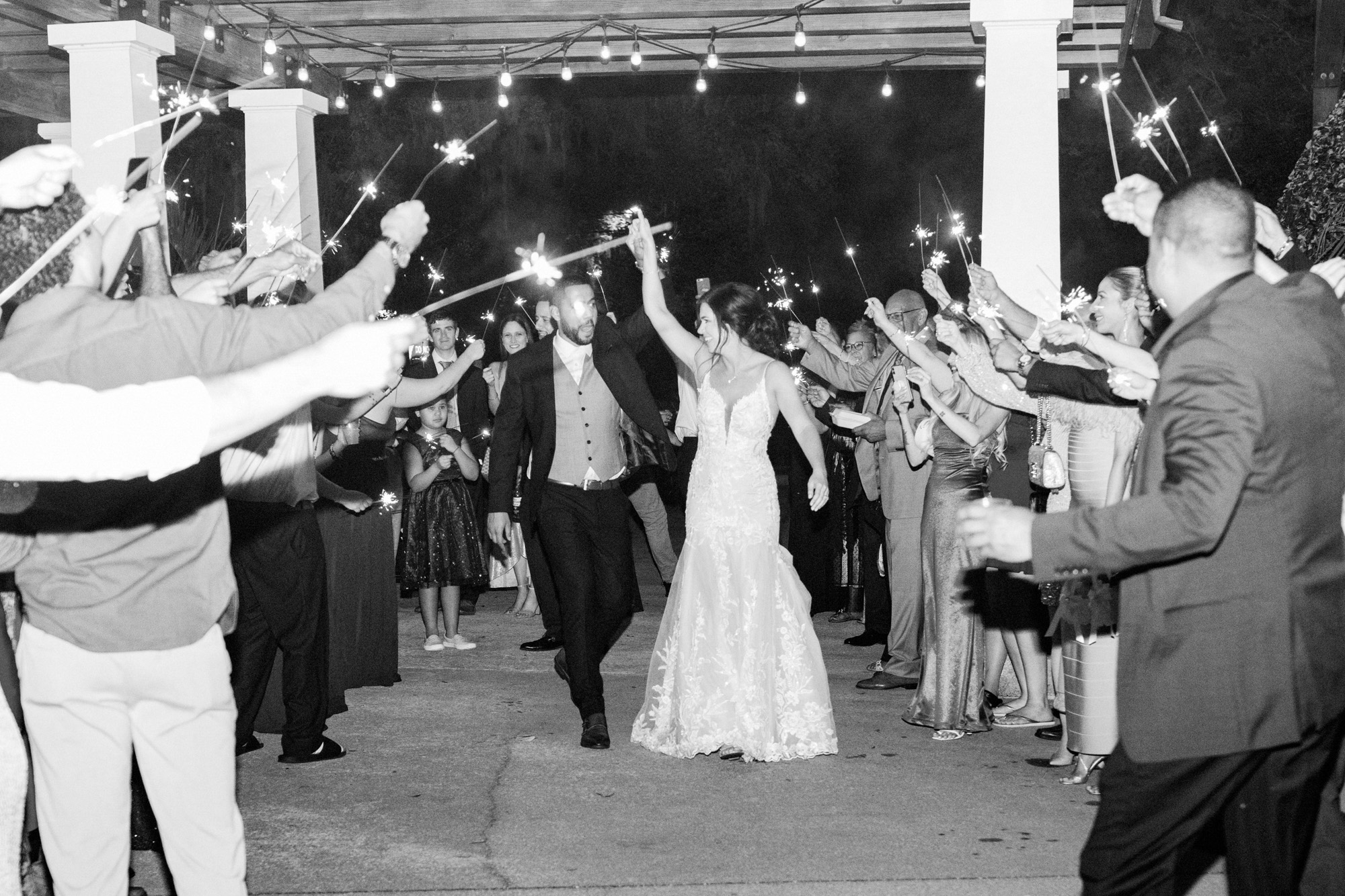 Newlyweds walking through a sparkler exit surrounded by wedding guests at night.