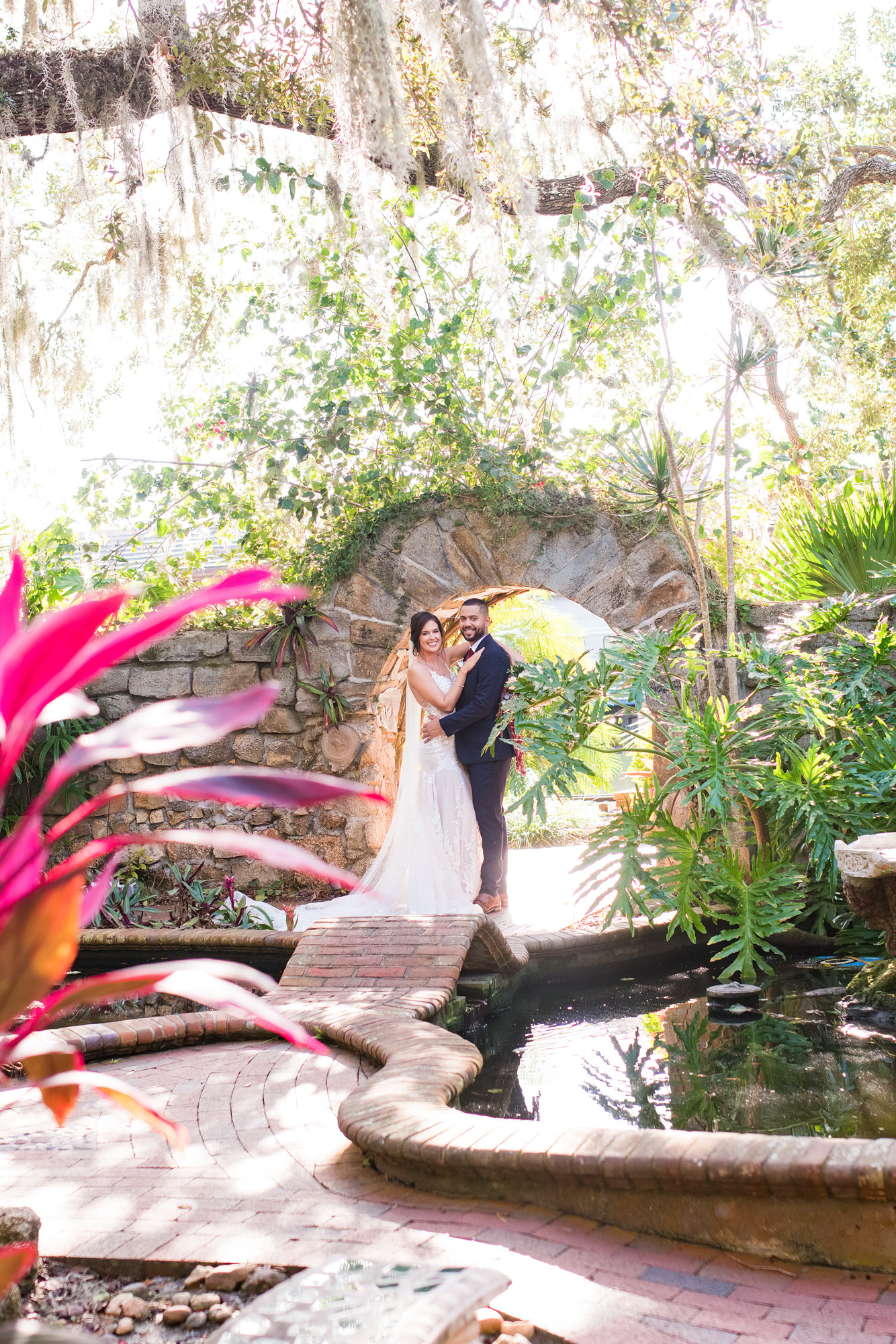 Bride and groom posing beneath a stone arch in the lush gardens at Estate on the Halifax.