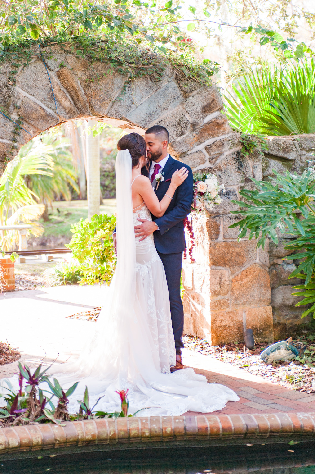 Bride and groom kissing beneath a stone arch in the gardens at Estate on the Halifax.