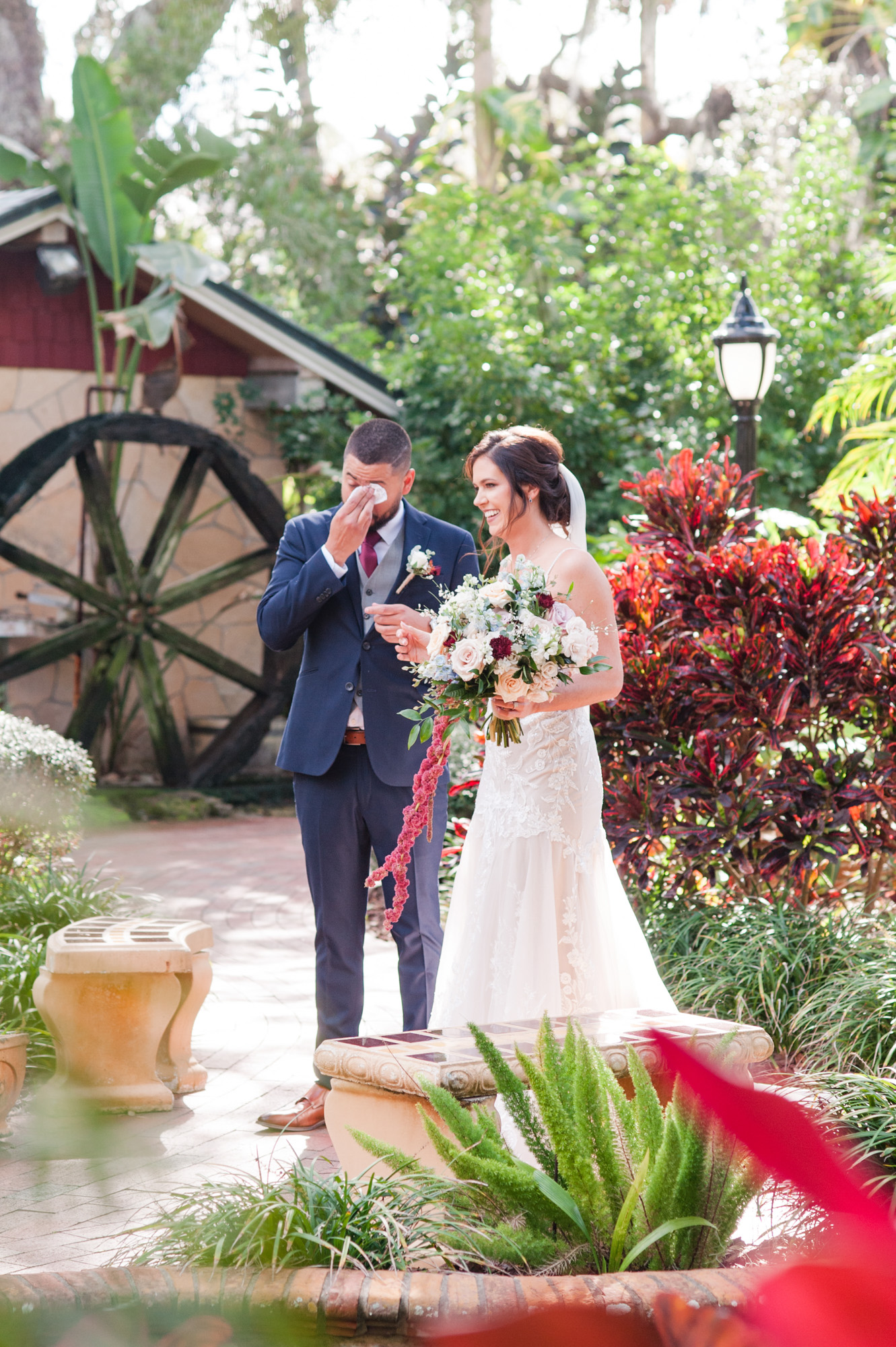 Groom wiping away tears while standing with the bride in the garden after their wedding portraits.