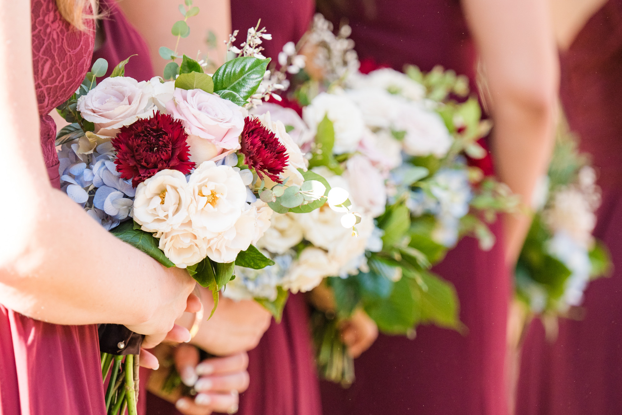 Close-up of bridesmaids holding blush, burgundy, white and blue wedding bouquets.