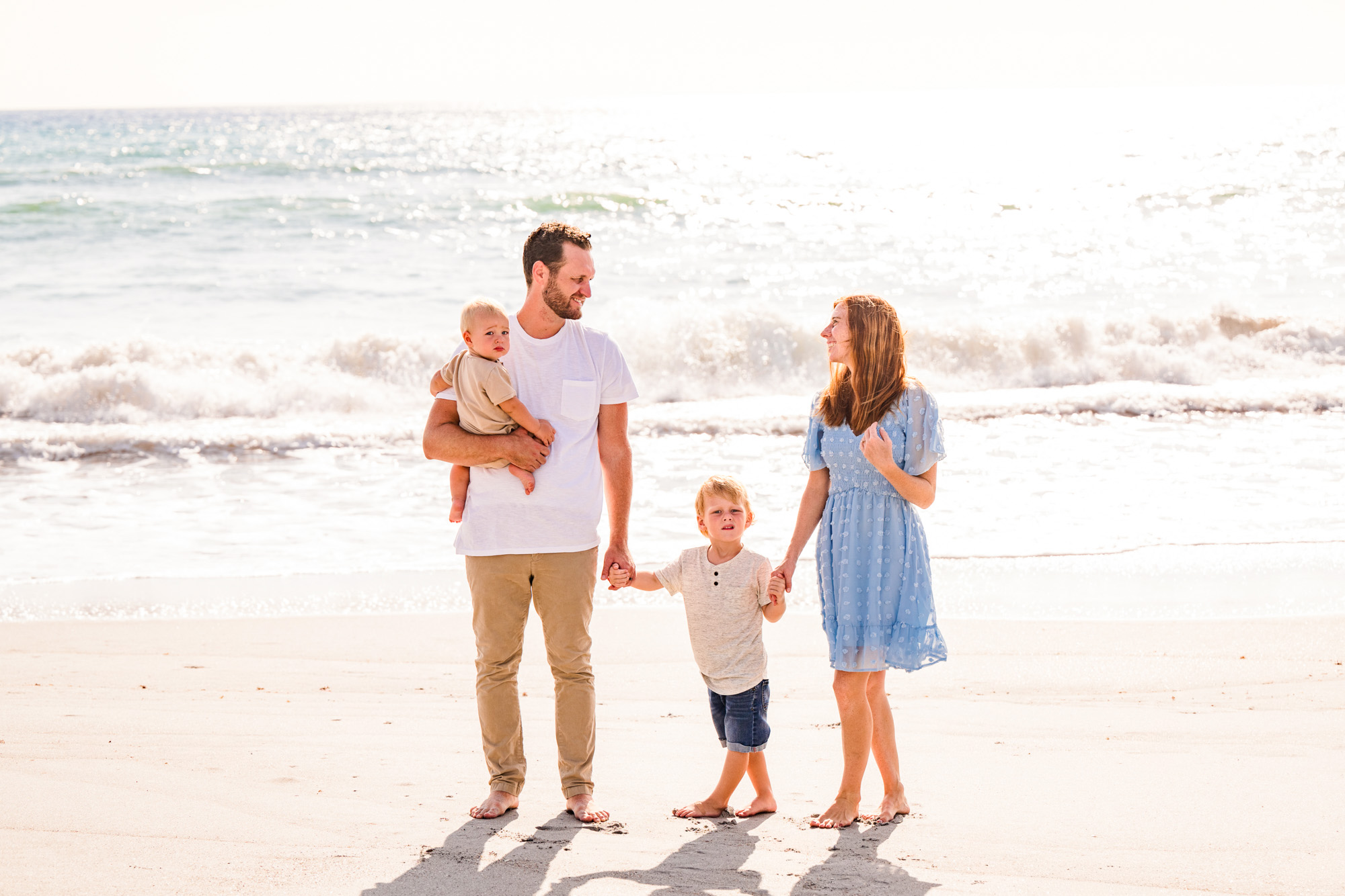Family holding hands walking on beach during sunrise