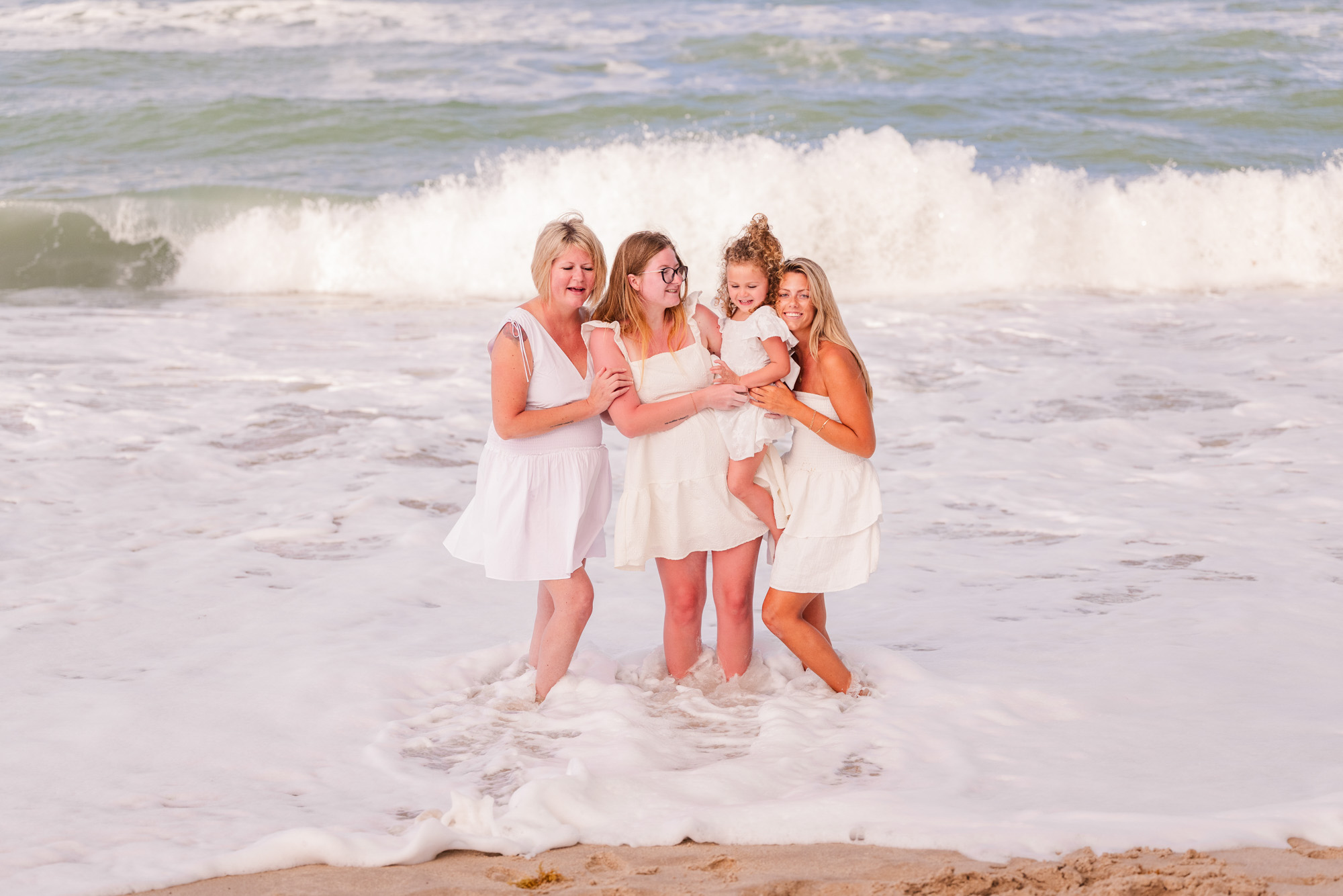 Group of four generations of women dressed in all white standing in the ocean during their Melbourne Beach family session