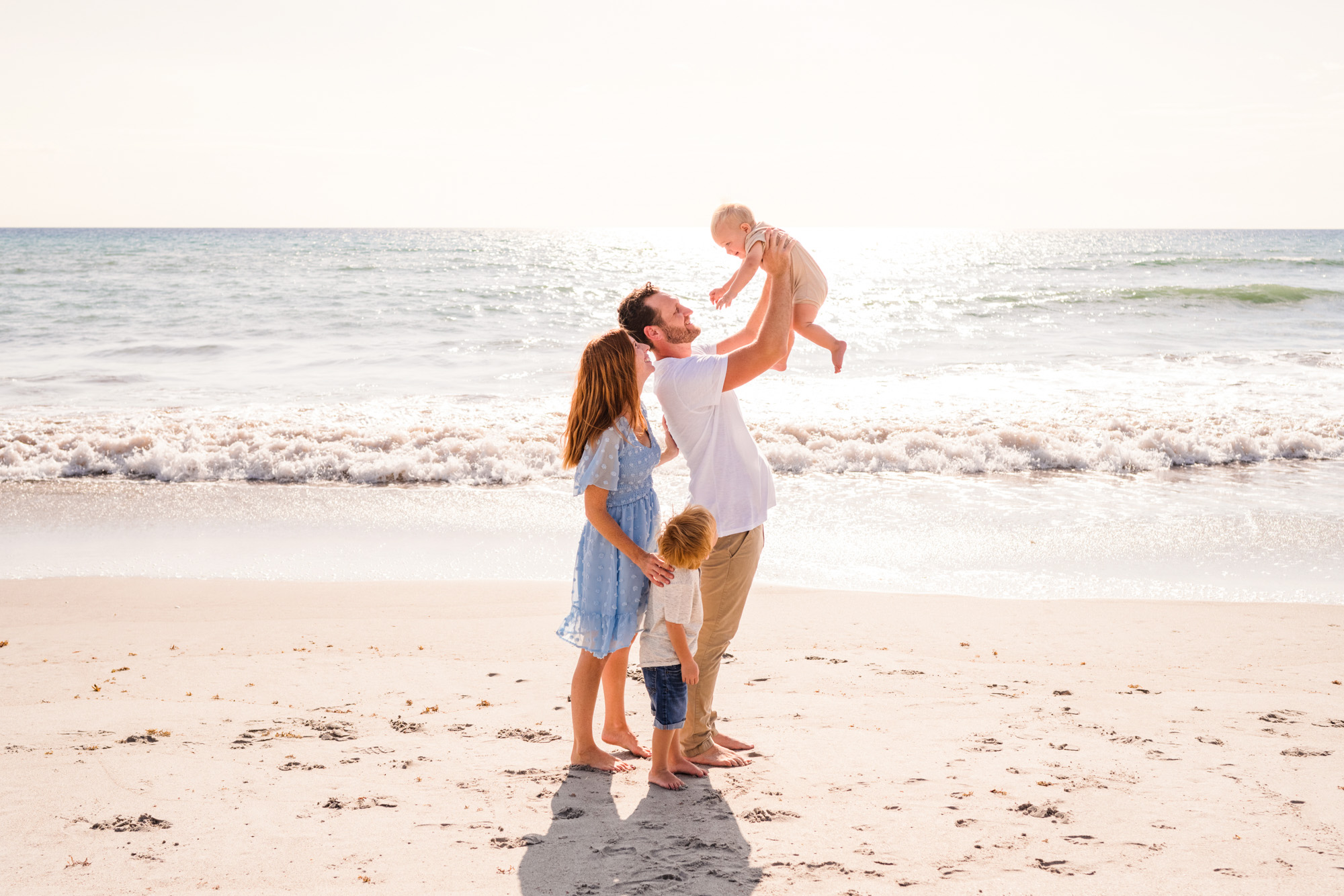 Dad lifting baby in the air with the sun rising in above the Atlantic Ocean