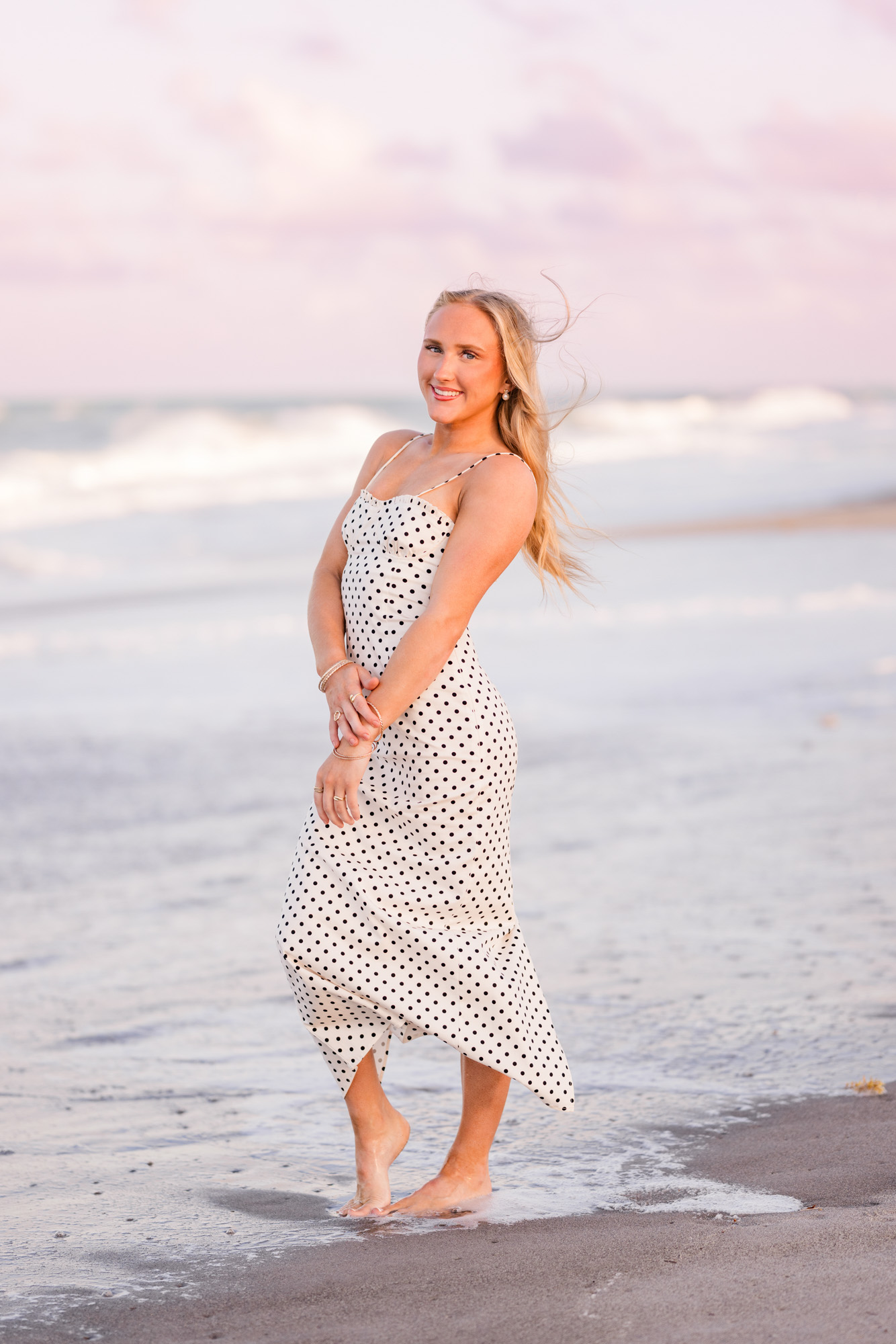 High school senior standing with arms crossed as her hair blows in the wind on Melbourne Beach
