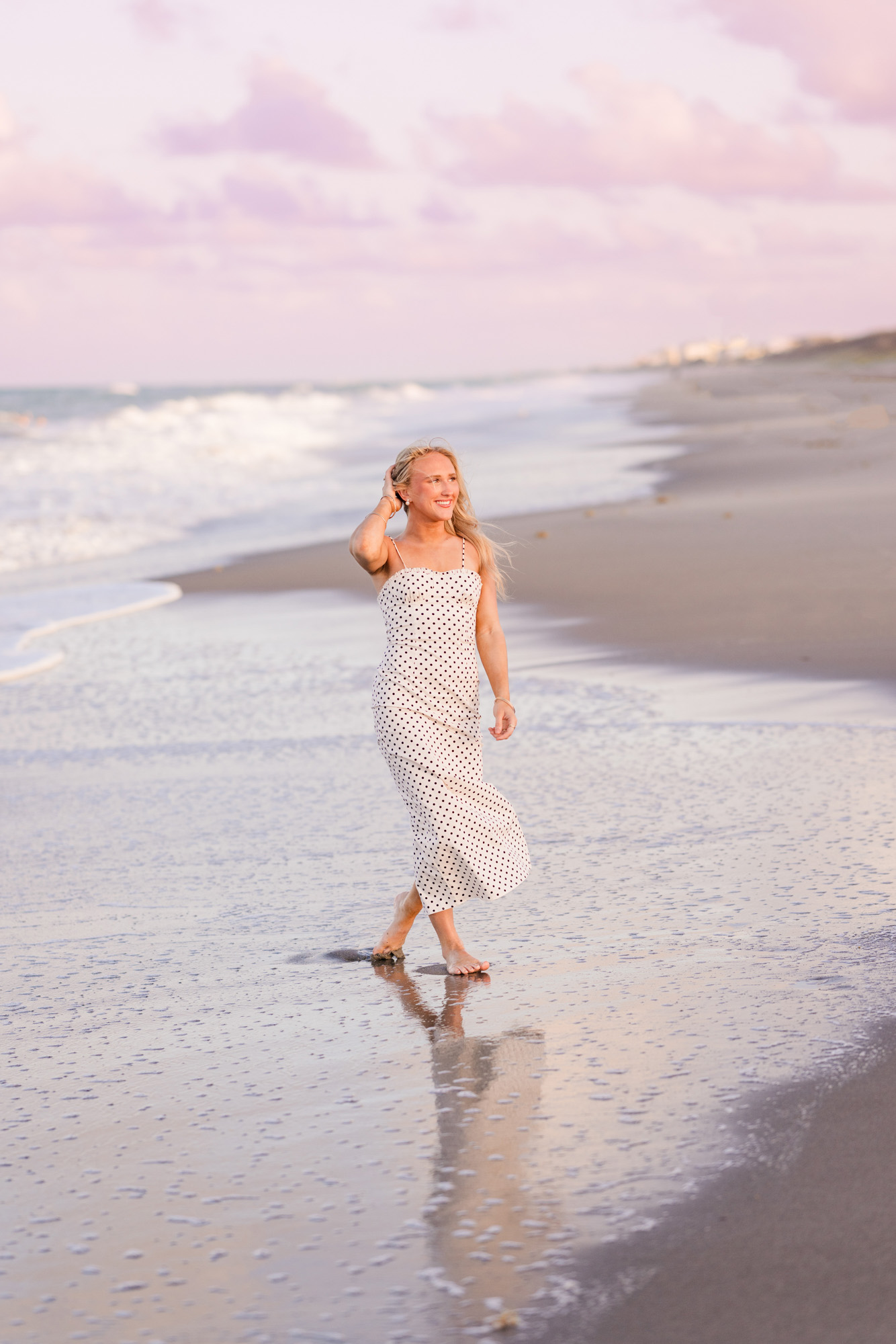 High school senior holding hair back from wind walking down Melbourne Beach