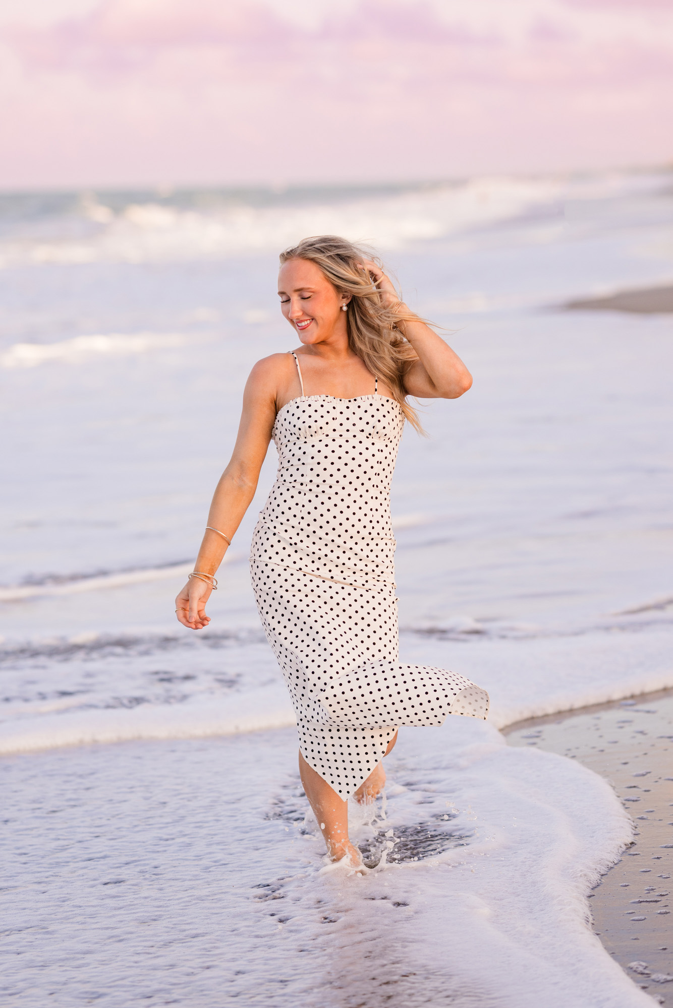High school senior in long white dress walking through the waves of the ocean on Melbourne Beach