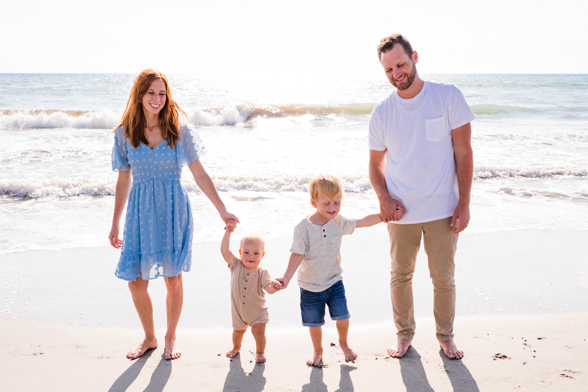 Mom and Dad holding kids hands with the sun rising behind them on Melbourne Beach during a family session