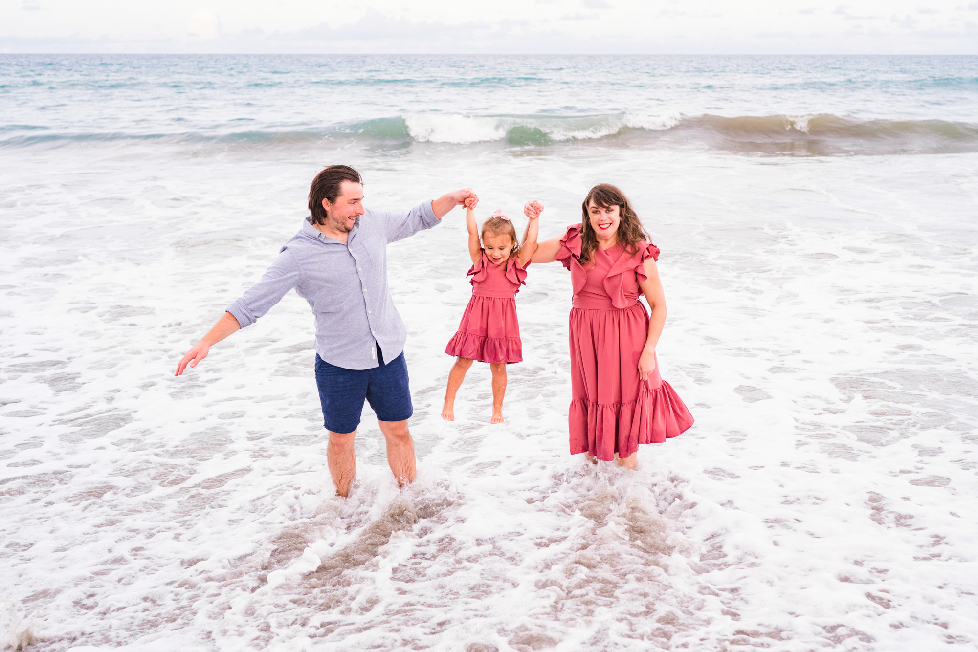 family of three swinging little girl while in the waves of the Atlantic Ocean