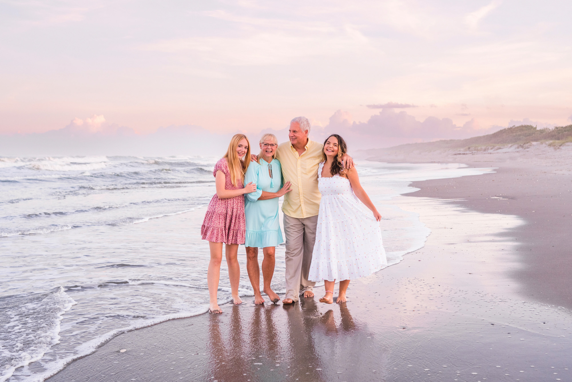 Family of four with two grown girls dressed in warm pastels on Melbourne Beach, Florida during their family session
