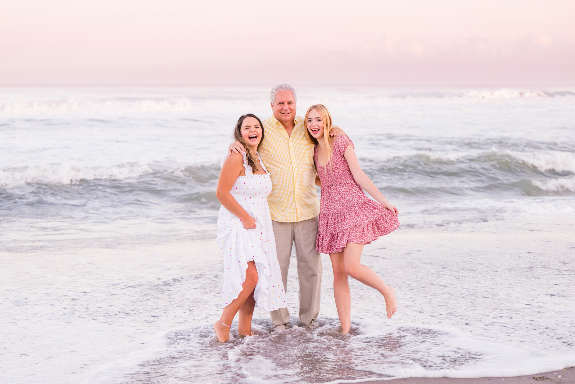 Two daughters with arms around their father splashing in the water