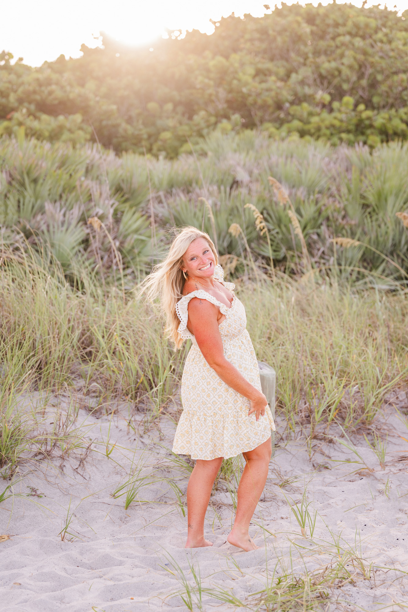woman in white standing near the dunes while the wind pushes her hair back