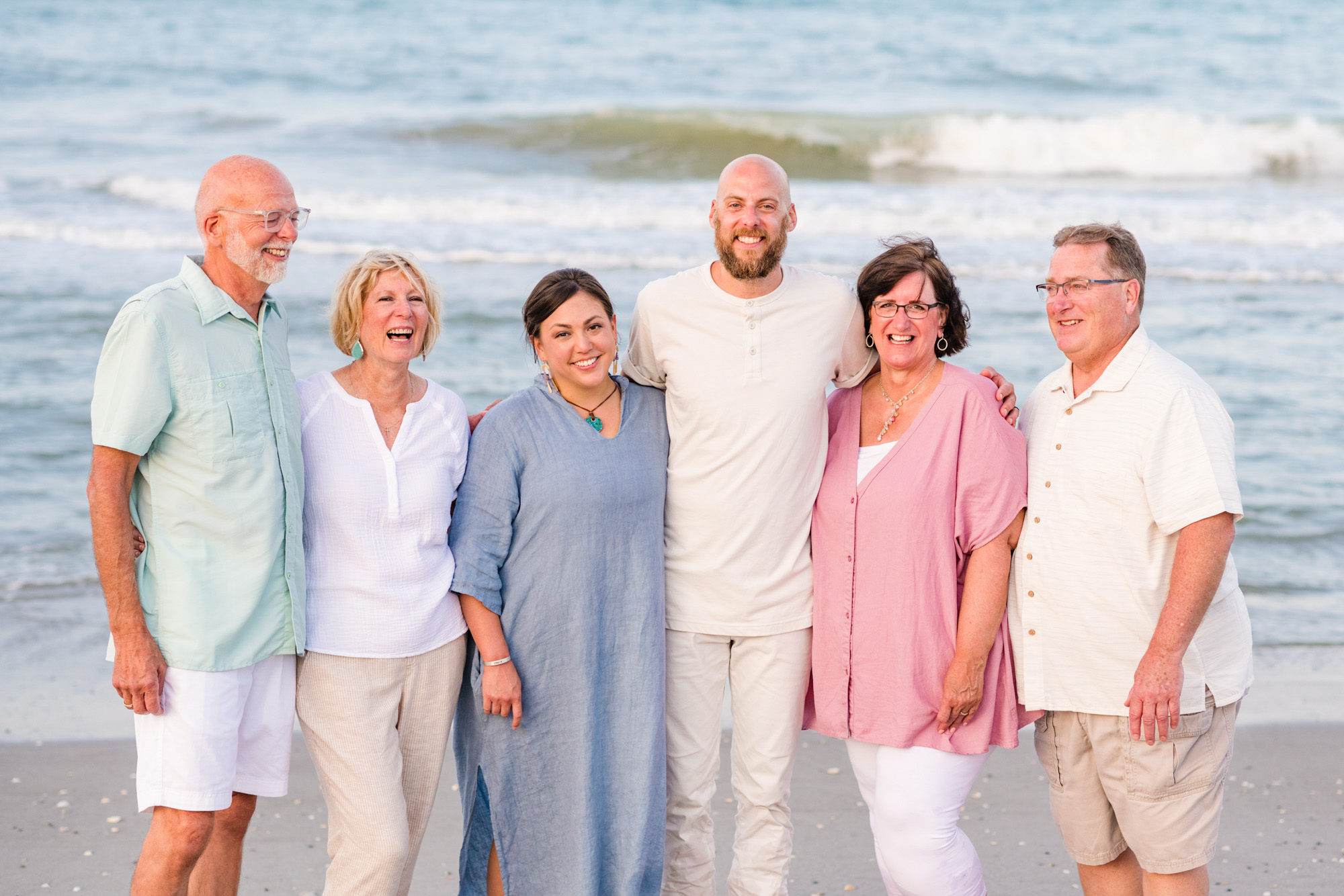 Family dressed in soft pastels all standing together by the edge of the water