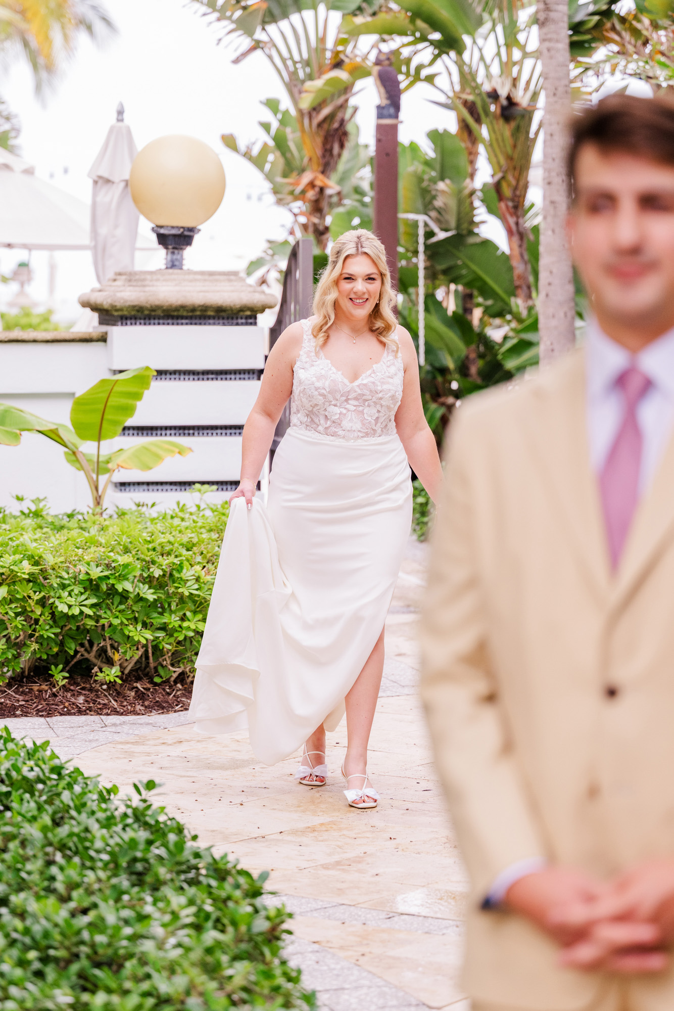 Bride walks toward the groom during their wedding first look in a tropical courtyard at Vero Beach Hotel and Spa.