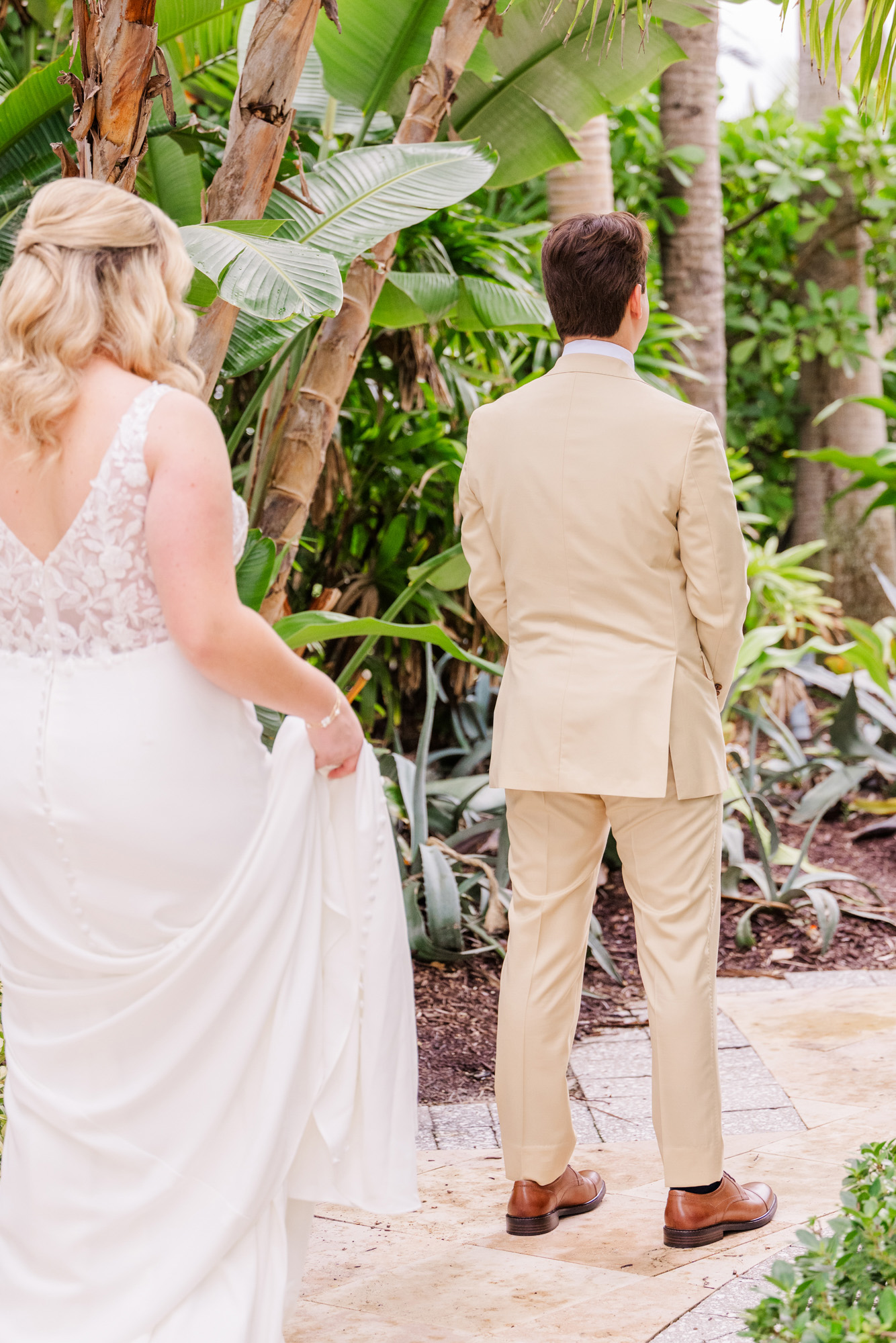 Bride approaches groom from behind for their wedding first look among tropical greenery.