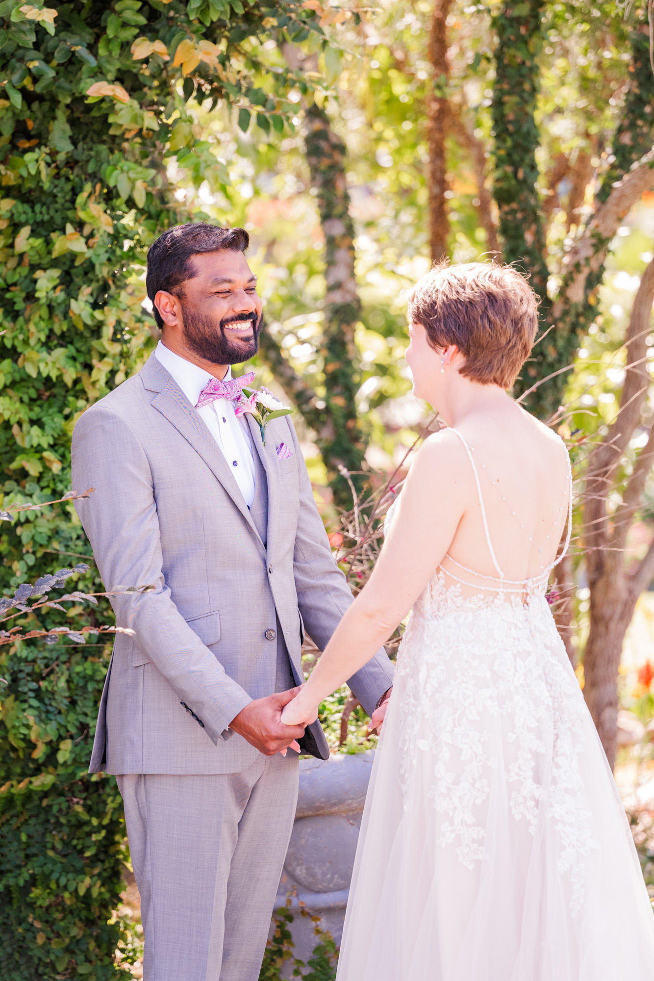 Groom smiles at the bride while they hold hands during their wedding first look.
