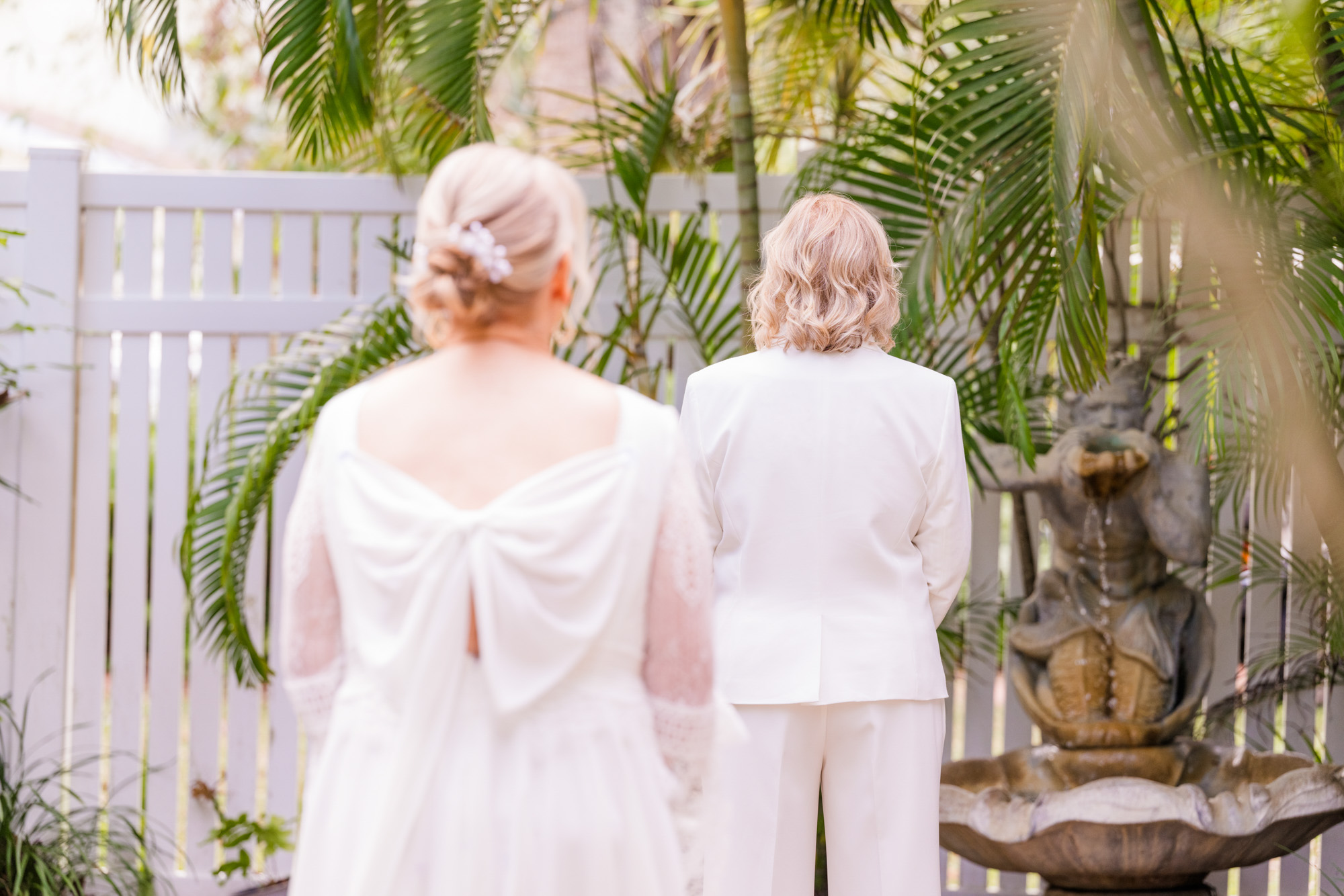 Bride approaches her partner from behind before their wedding first look in a tropical garden.