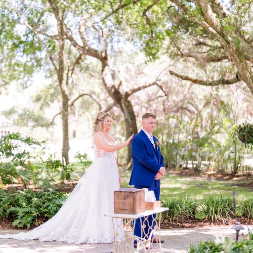 Bride reaches toward the groom in a blue suit moments before their outdoor wedding first look at Up the Creek Farms Wedding.