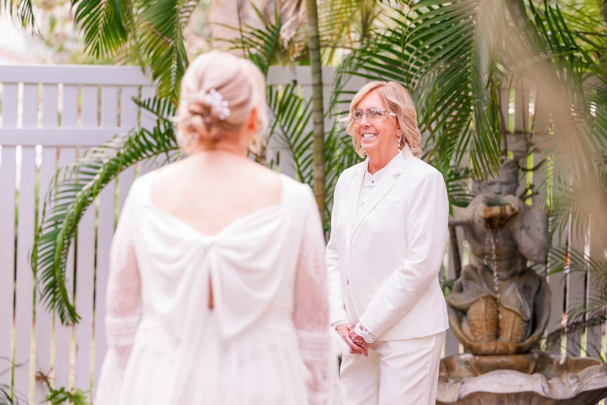 wo brides see each other for the first time on their wedding day surrounded by palm trees.