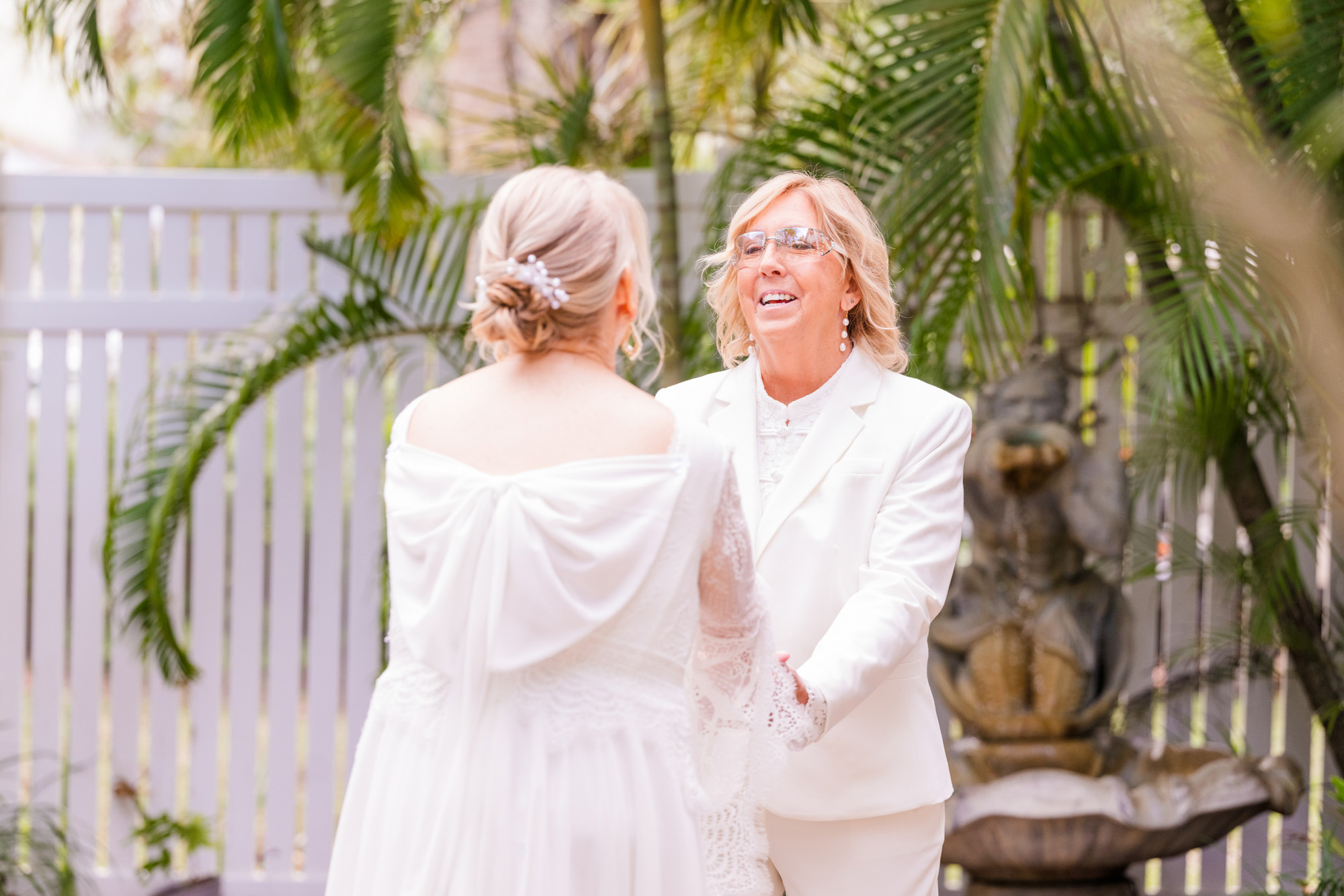 wo brides hold hands after their wedding first look beneath tropical palm trees.