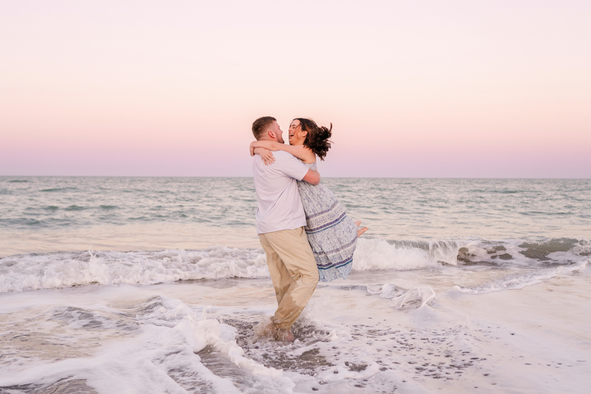 Man lifting woman in floral dress in the ocean during their Melbourne beach engagement session