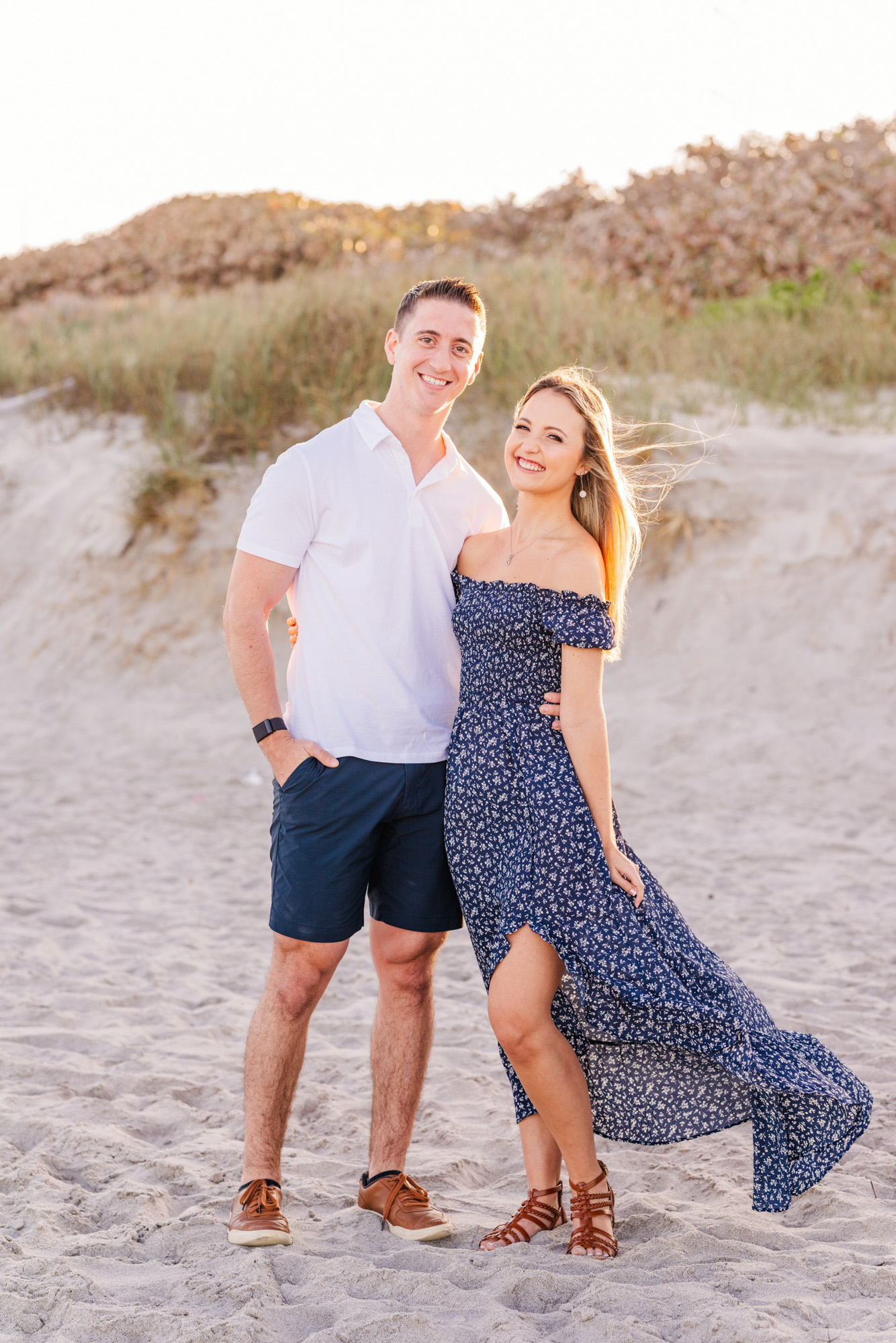 Man standing with arms around woman wearing a blue dress blowing in the wind