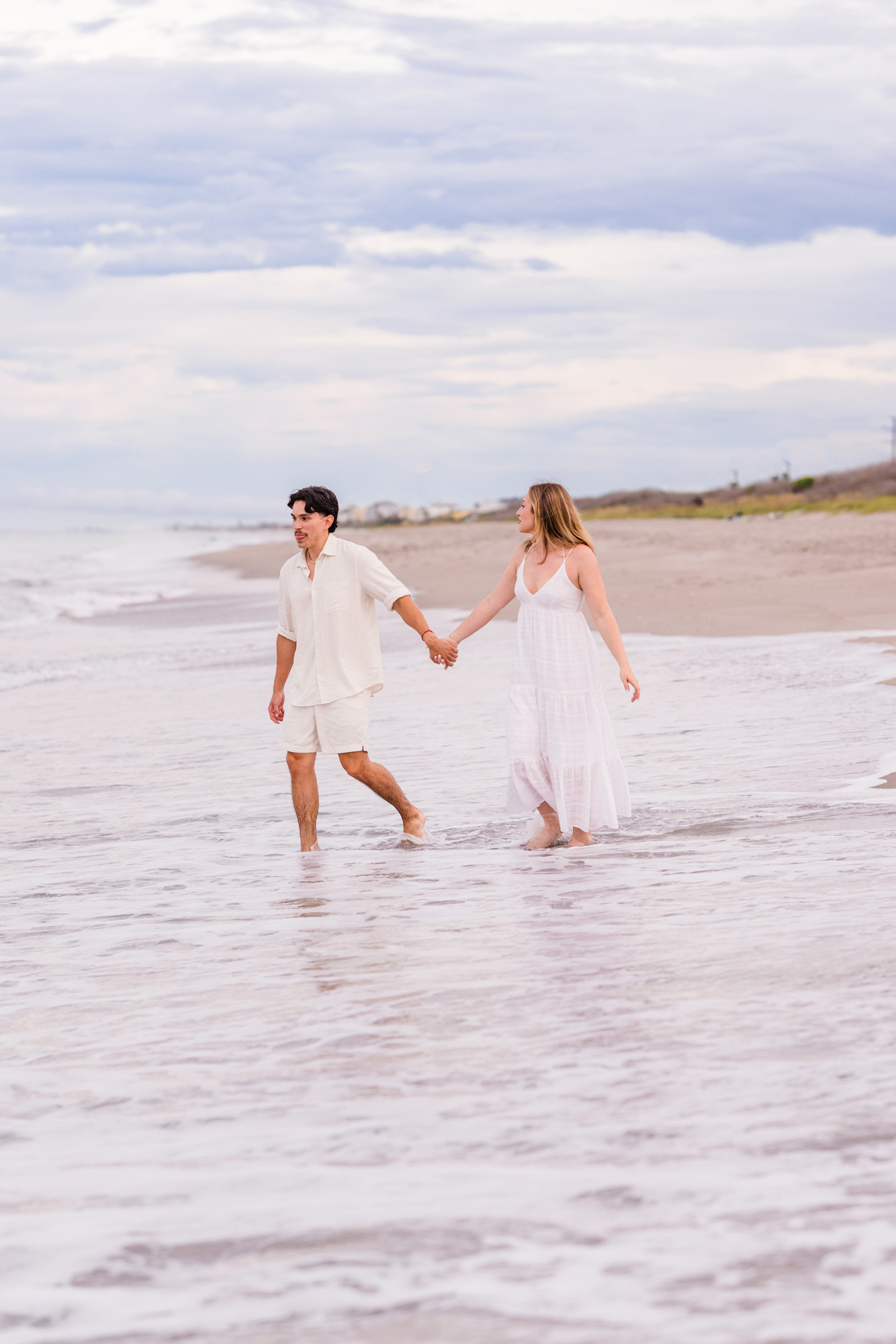 couple both dressed in white holding hands while running in the water on Melbourne Beach