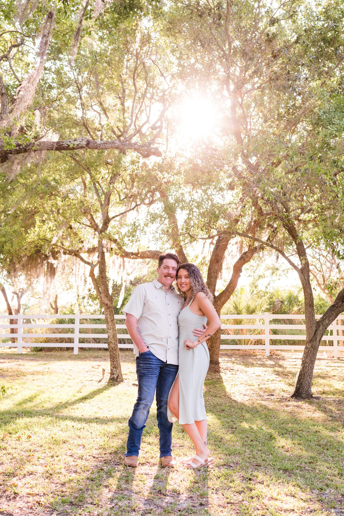 Man and woman standing with sunburst shining through the Oak trees at their Up the Creek Farms engagement session