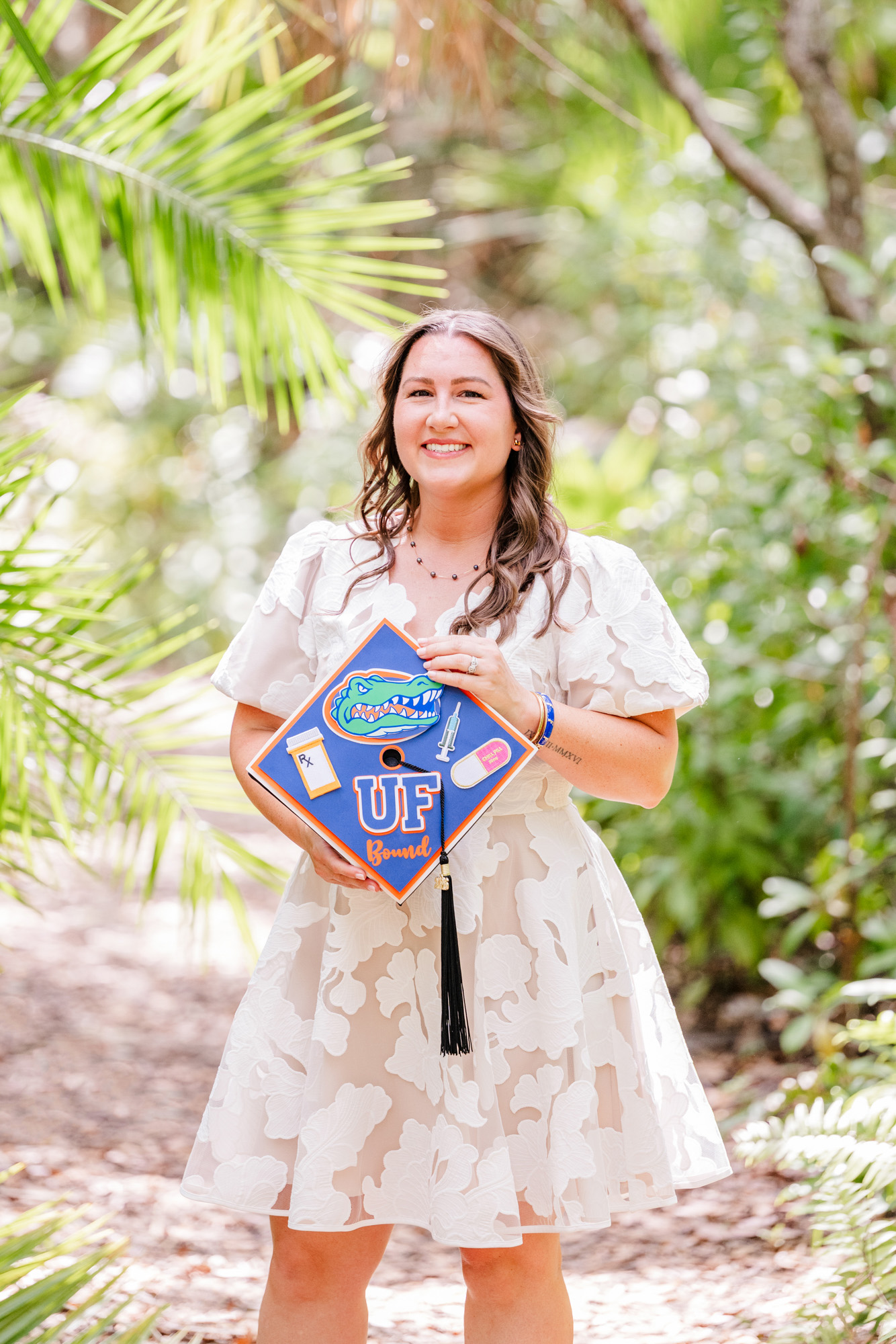 Graduate holding a decorated blue-and-orange cap at the Florida Tech Botanical Gardens.