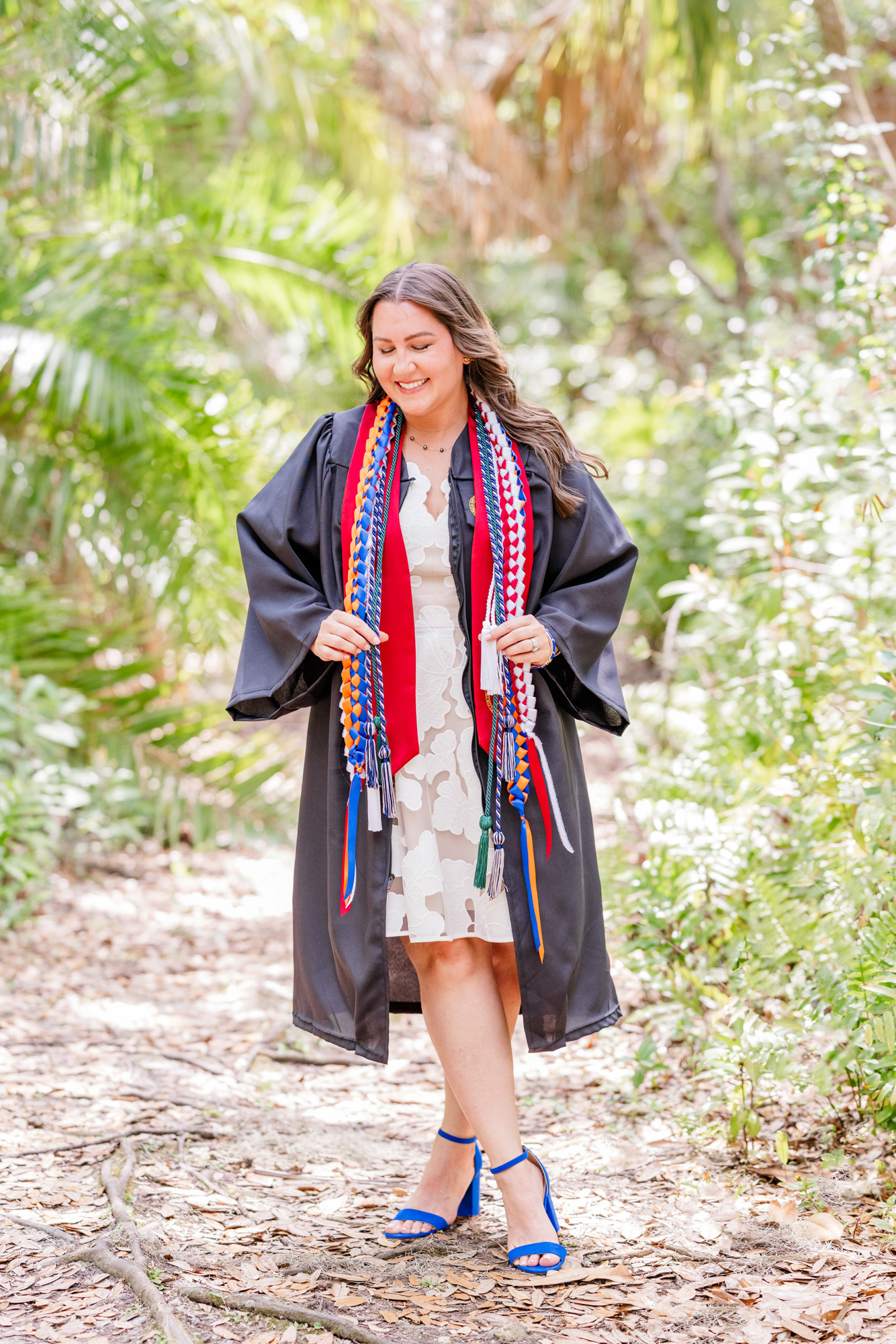 Graduate looking down and smiling while wearing her graduation gown and honor cords.