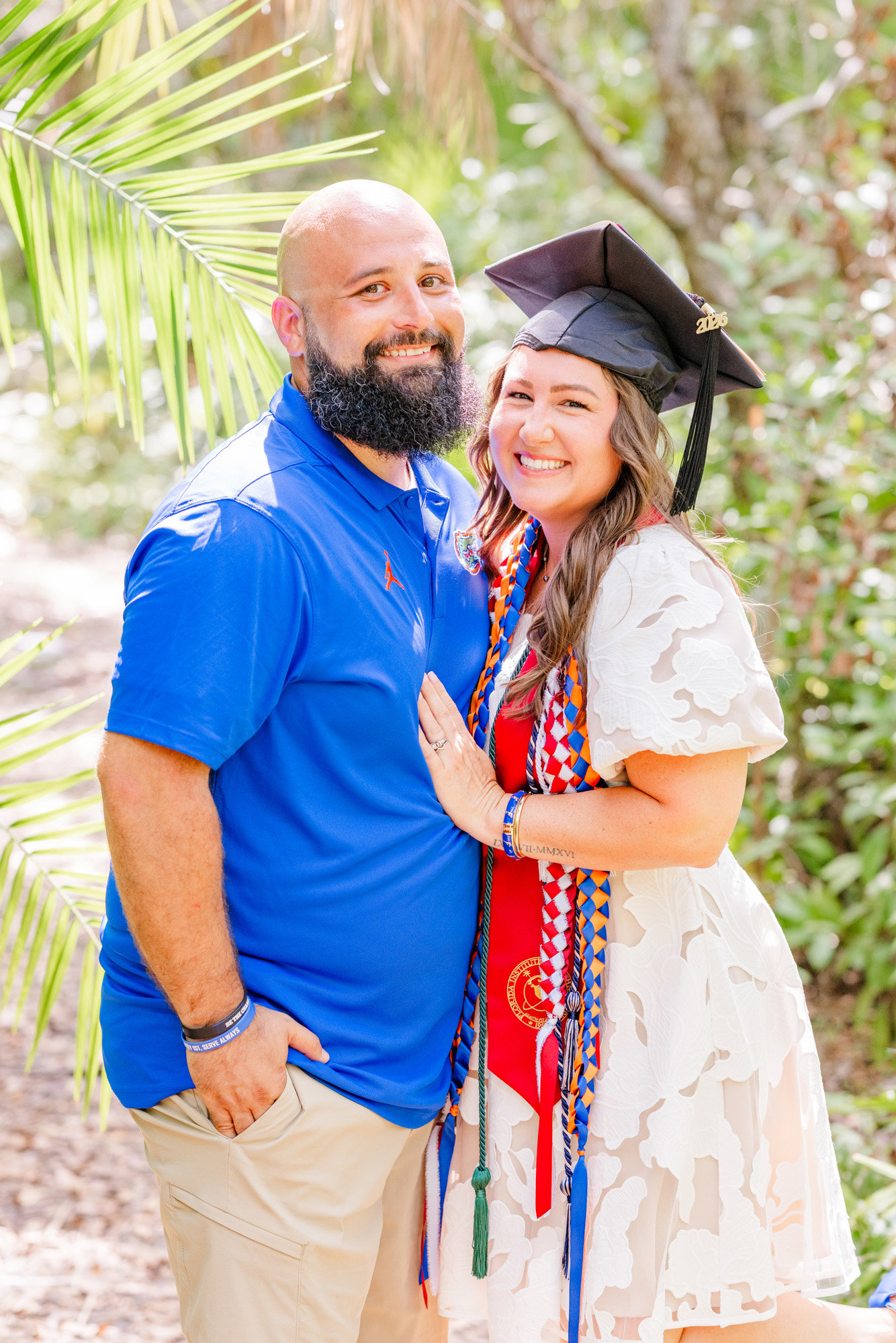 Graduate and her partner standing close together beneath the palm trees.