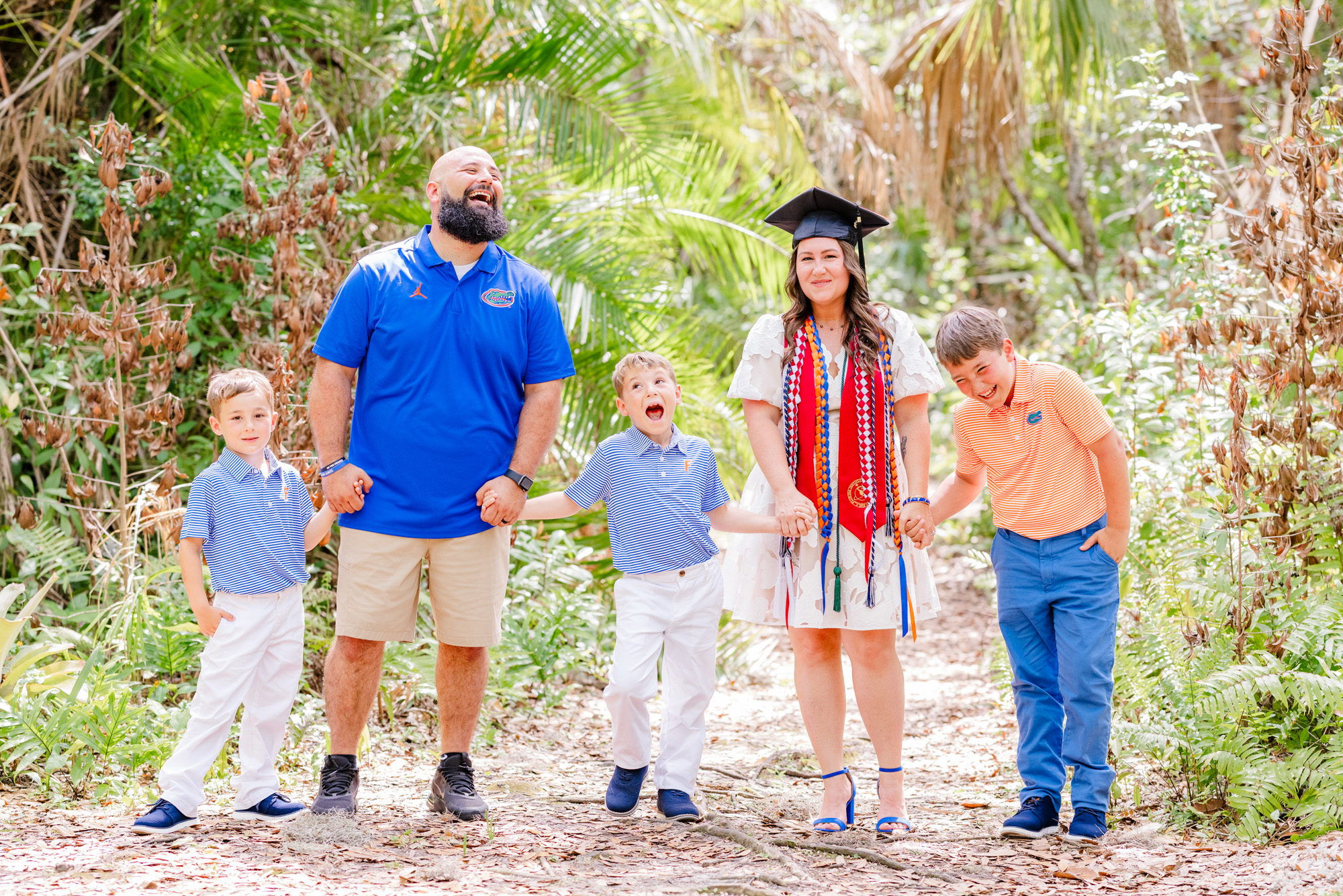 Family of five holding hands and laughing together on a garden path.